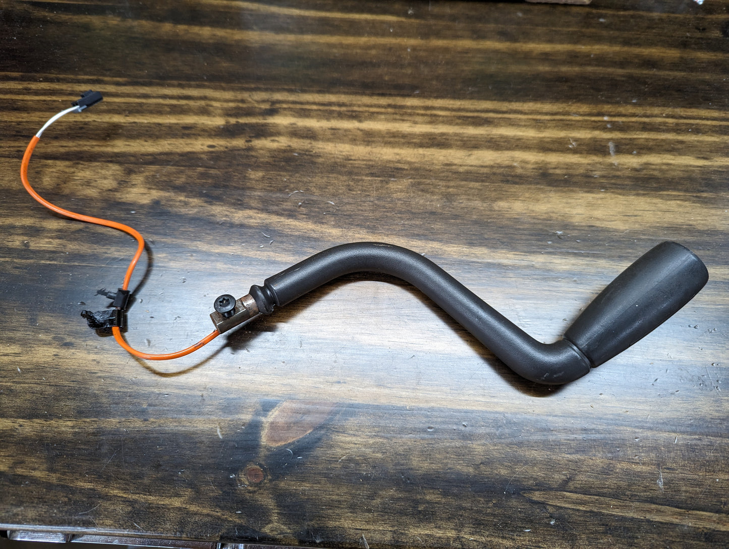 A black, L-shaped General Motors OEM Column Shift Lever with Tow/Haul for 1999-2006 GM Full Size Trucks, featuring an orange and black wire, lies on a wooden surface with a connector at one end and a rounded tip at the other.