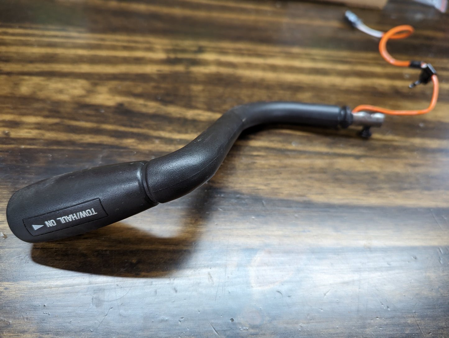 A black turn signal indicator with TURN/TAIL ON written on it, featuring an orange wire, sits on a wooden surface. Its style resembles the General Motors OEM Column Shift Lever with Tow/Haul for 1999-2006 GM Full Size Trucks.