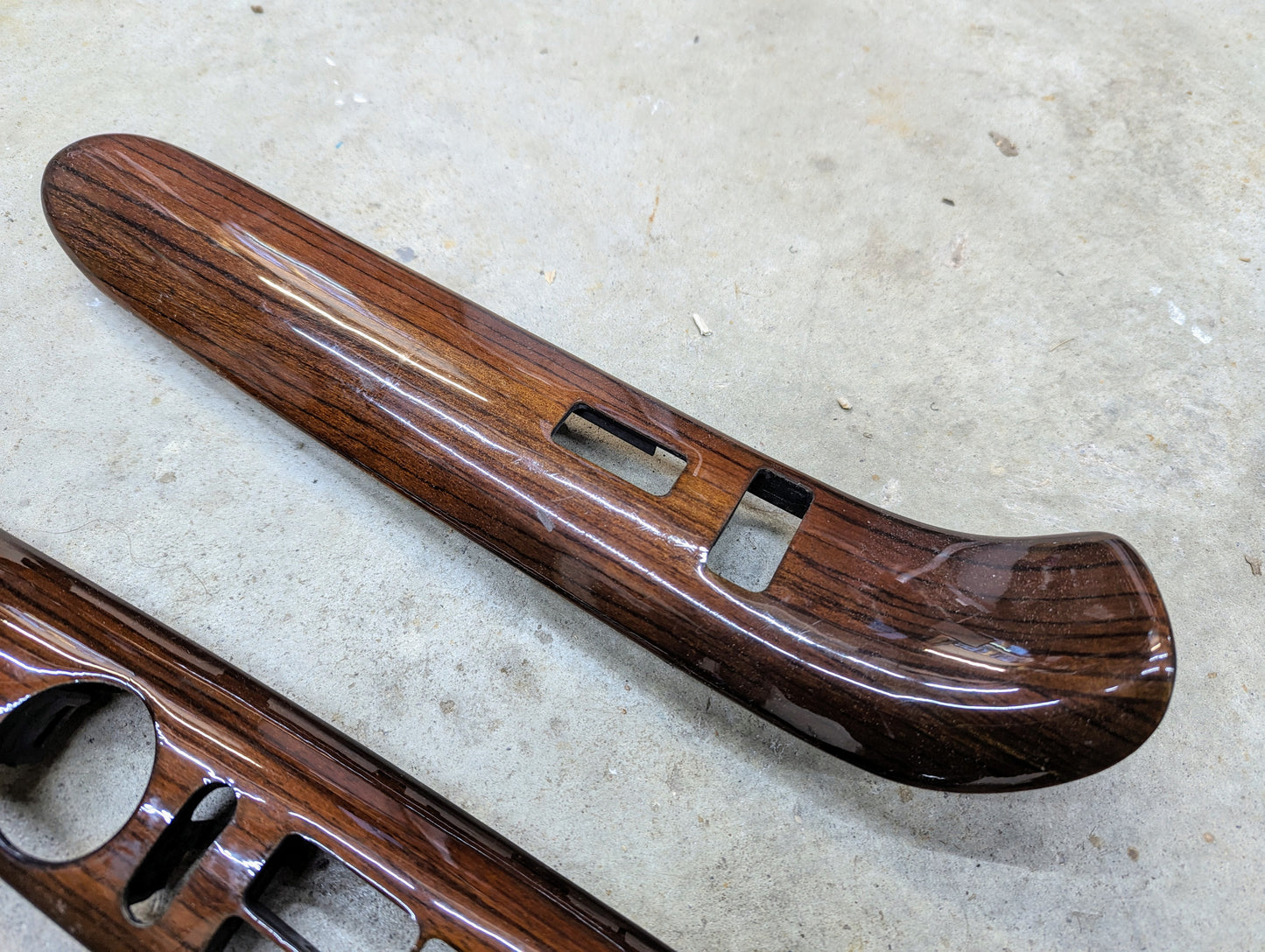 The General Motors OEM Woodgrain Pair LH RH Power Switch Bezel for 1999-2000 Escalade Denali and more, features switch cutouts and is shown resting on a light gray concrete surface.
