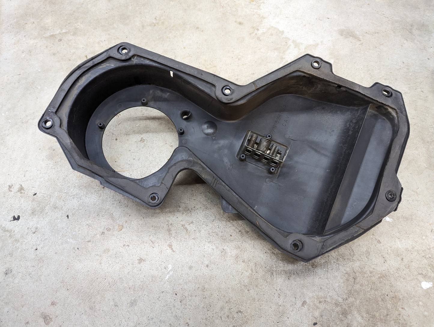 The General Motors OEM HD Heater A/C Delete with Control Panel for 1994 Chevy S10 & GMC Sonoma, made of black plastic with mounting holes and a large opening, is shown resting on concrete.