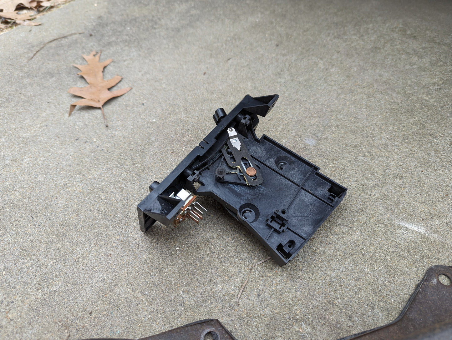 A General Motors OEM A/C Delete Heater Box & Control Panel for 1982-1985 S10, Blazer, and more sits on a concrete surface outdoors with exposed wiring; a brown, dried oak leaf appears in the background.