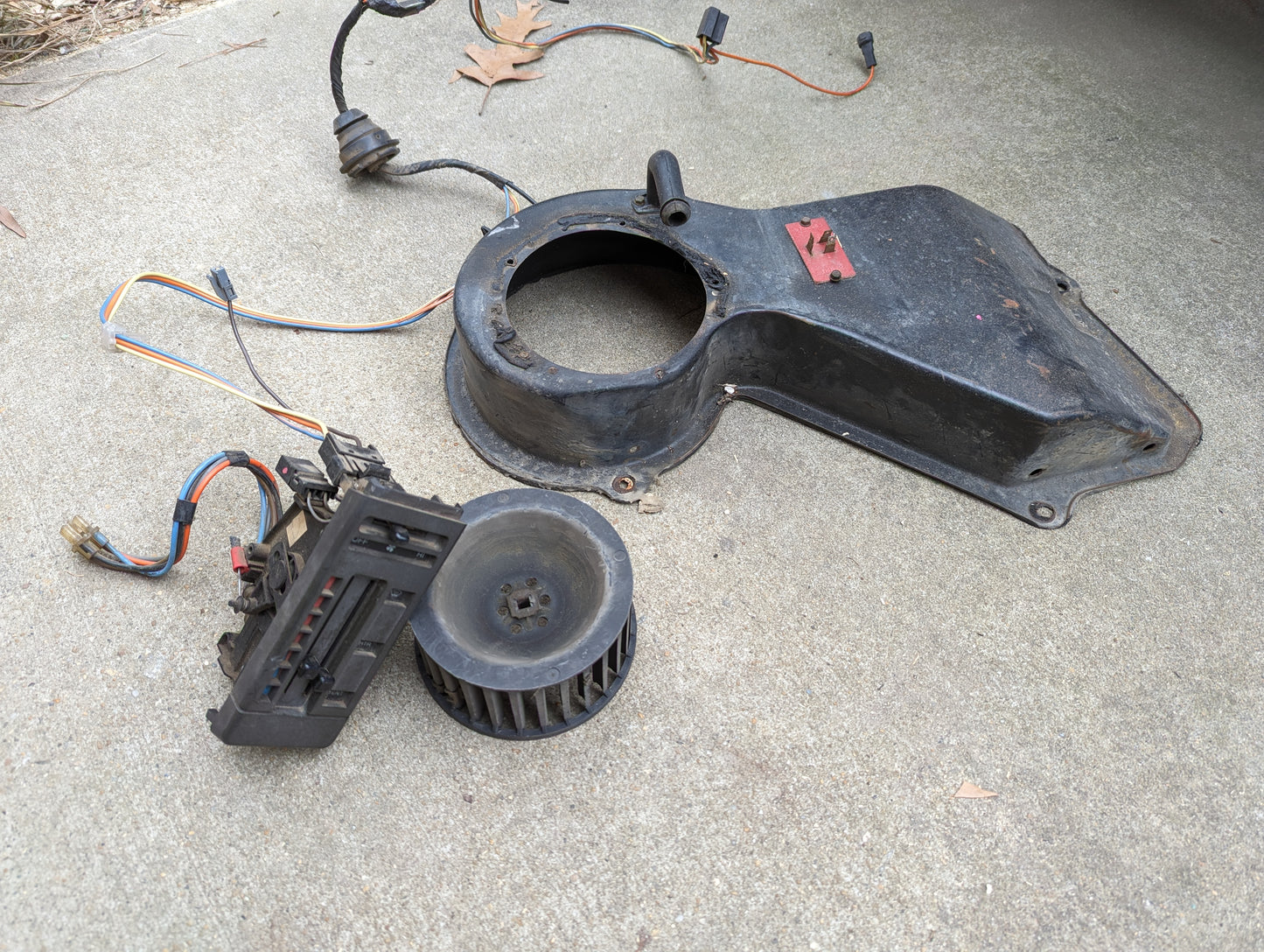 General Motors OEM A/C Delete Heater Box & Control Panel Swap Parts for 1986-1994 S10, Blazer, and more—includes housing, blower wheel, resistor, and wiring—are shown on concrete with a dry leaf; perfect for your custom project.