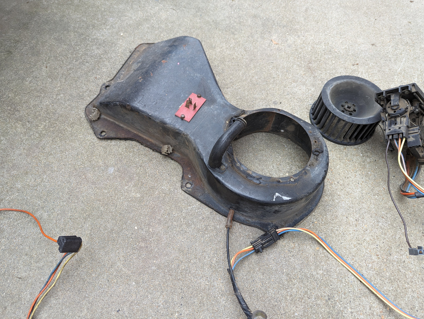 A General Motors OEM A/C Delete Heater Box & Control Panel Swap for 1986-1994 S10, Blazer, and more sits on concrete with wiring, a blower fan, and electrical components.