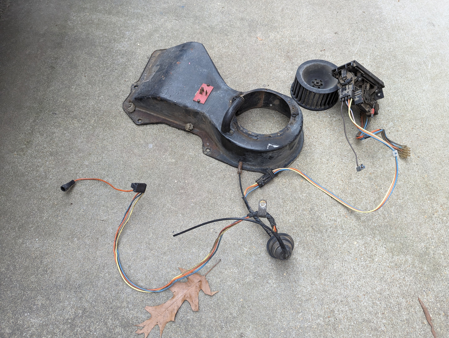 OEM A/C Delete Heater Box & Control Panel Swap Parts by General Motors for 1986-1994 S10, Blazer, and more—includes plastic cover, blower fan, wiring, and connectors—are arranged on concrete with a brown oak leaf nearby.