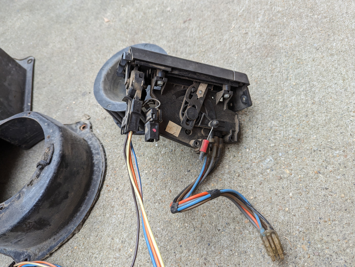 A close-up of the General Motors OEM A/C Delete Heater Box & Control Panel Swap Parts for 1986-1994 S10 and Blazer, showing colored wires and connectors on a concrete surface with other dark plastic components nearby.