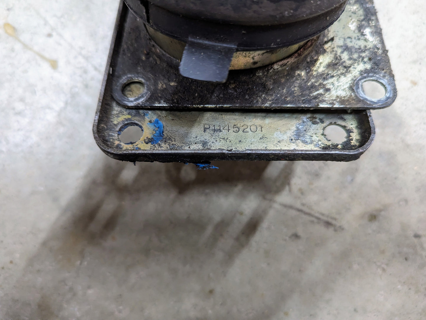 Close-up of a scratched, stained metal plate with four bolt holes, attached to a worn General Motors OEM T5 manual transmission shifter for 1982-1995 Chevy S10/Blazer; stamped code PM45201 visible at the bottom edge.