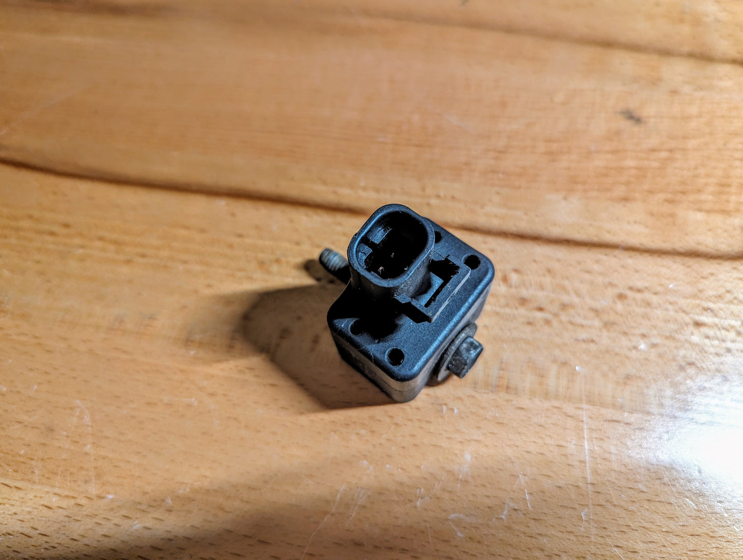 A General Motors TESTED Front Impact Air Bag Sensor (Part #15057507) for 2003-2004 GM Trucks, black plastic with two screws, is shown on a wooden surface from an overhead angle.