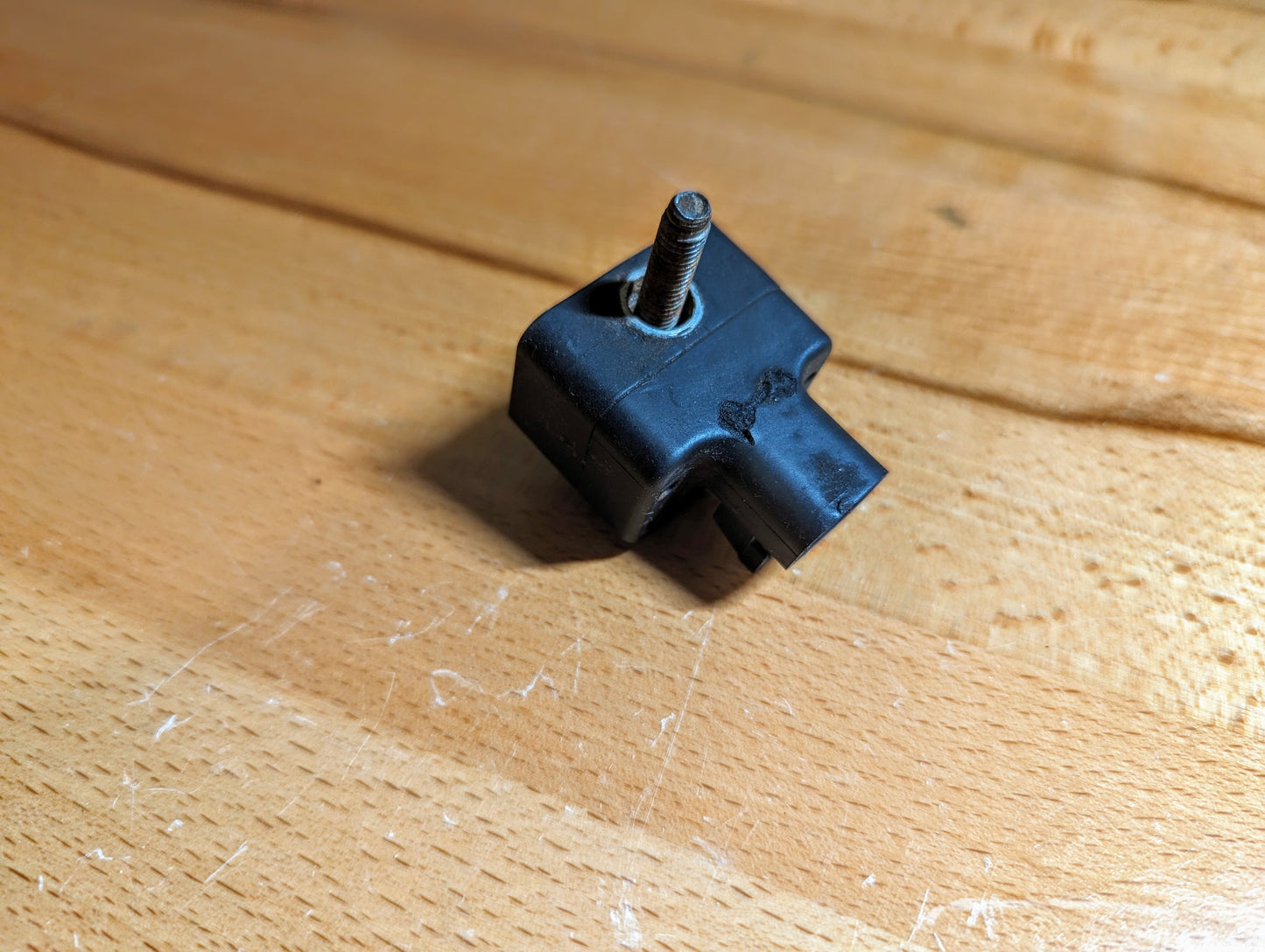 A TESTED General Motors Front Impact Air Bag Sensor (Part #15057507) for 2003-2004 GM Trucks, black plastic with a metal bolt and groove, lightly worn, rests on a light wood surface.