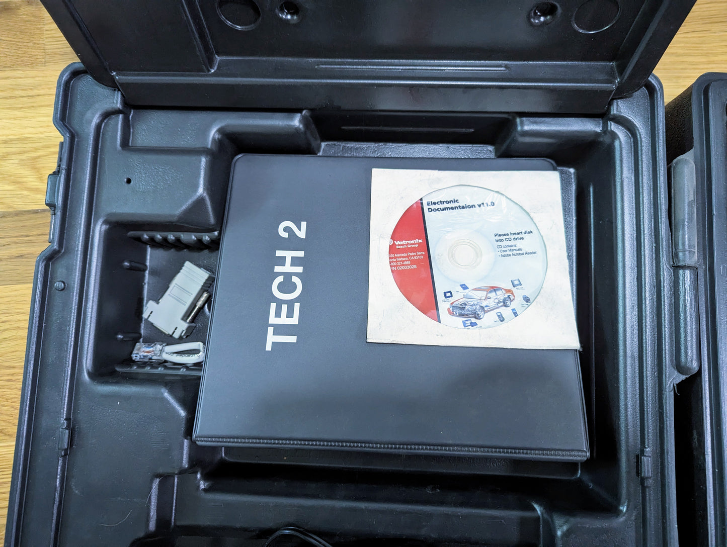 An open black Vetronix case containing a TESTED Tech 2 Automotive Diagnostic Tool & Accessories for 1991-2013 GM Vehicles, with data cable and Electronic Documentation v11.3 CD visible on a wooden surface. Perfect for GM diagnostics.