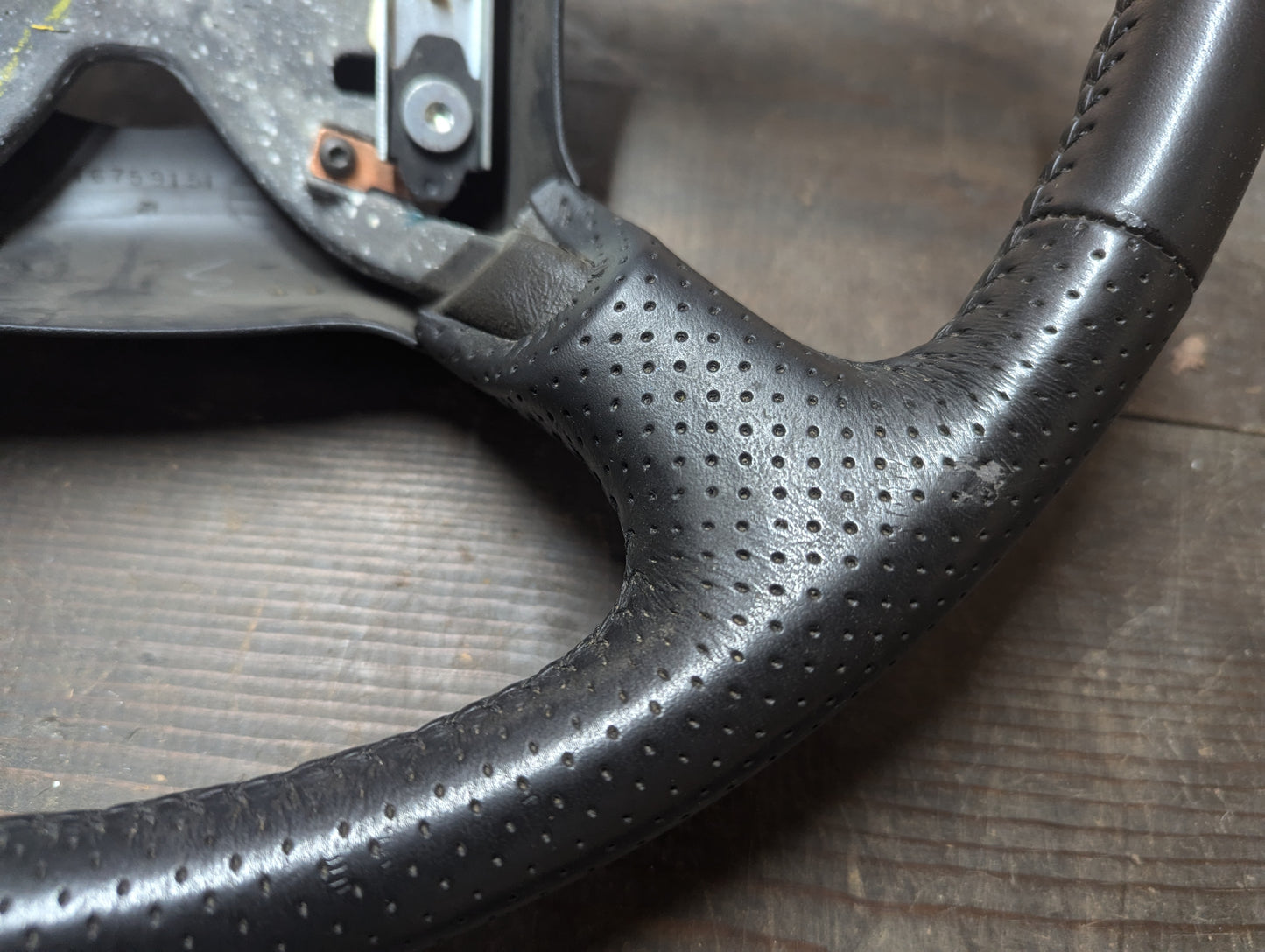 Close-up of a General Motors OEM Perforated Leather Steering Wheel for 1999-2005 Chevy Silverado S10 and more, showing some wear and scuffing, with a detailed leather texture on a wooden surface.