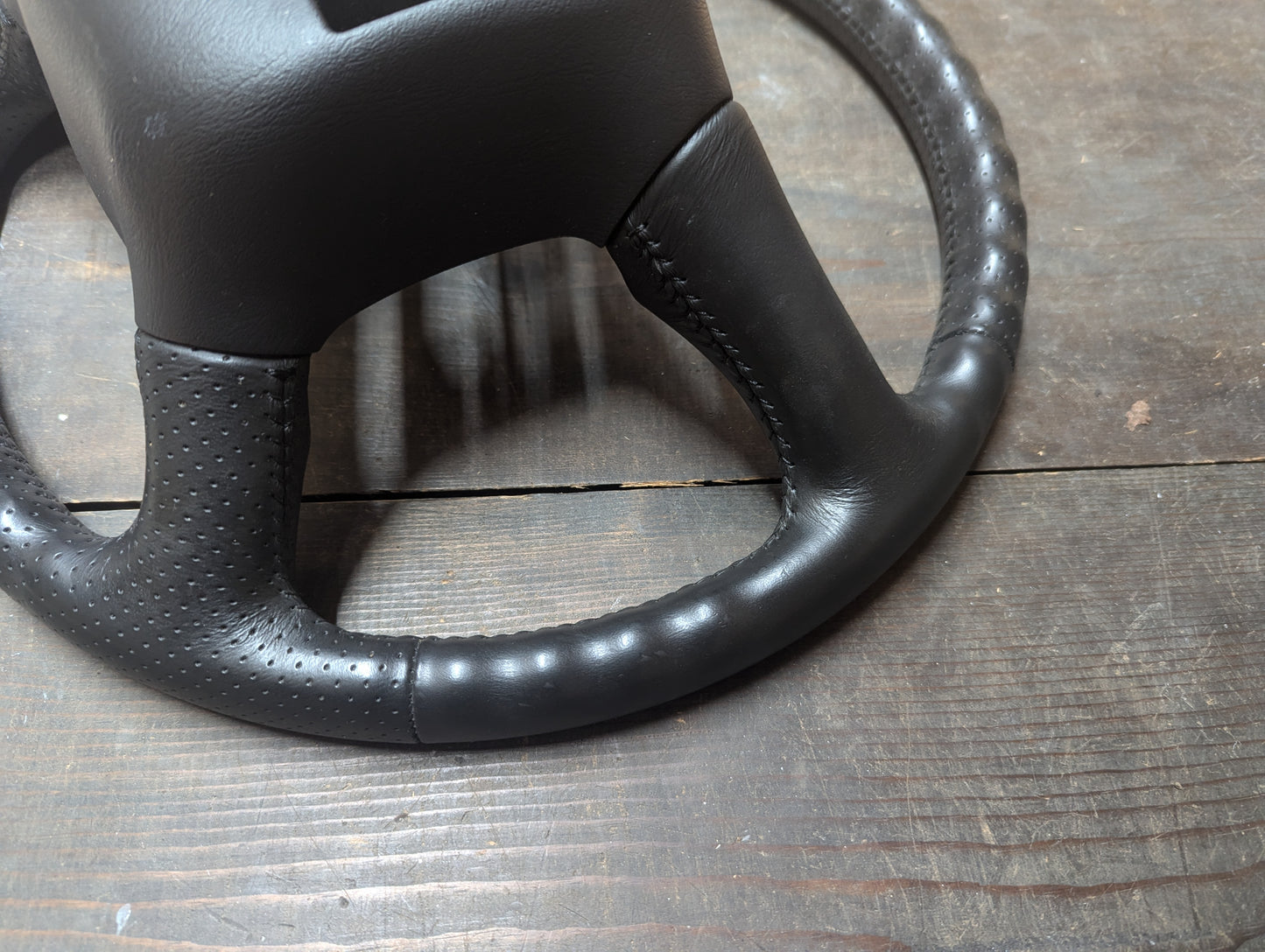 Close-up of an OEM perforated leather steering wheel by General Motors, showing textured and smooth sections with visible stitching—designed for 1999-2005 GM Chevy Silverado, S10, and more.
