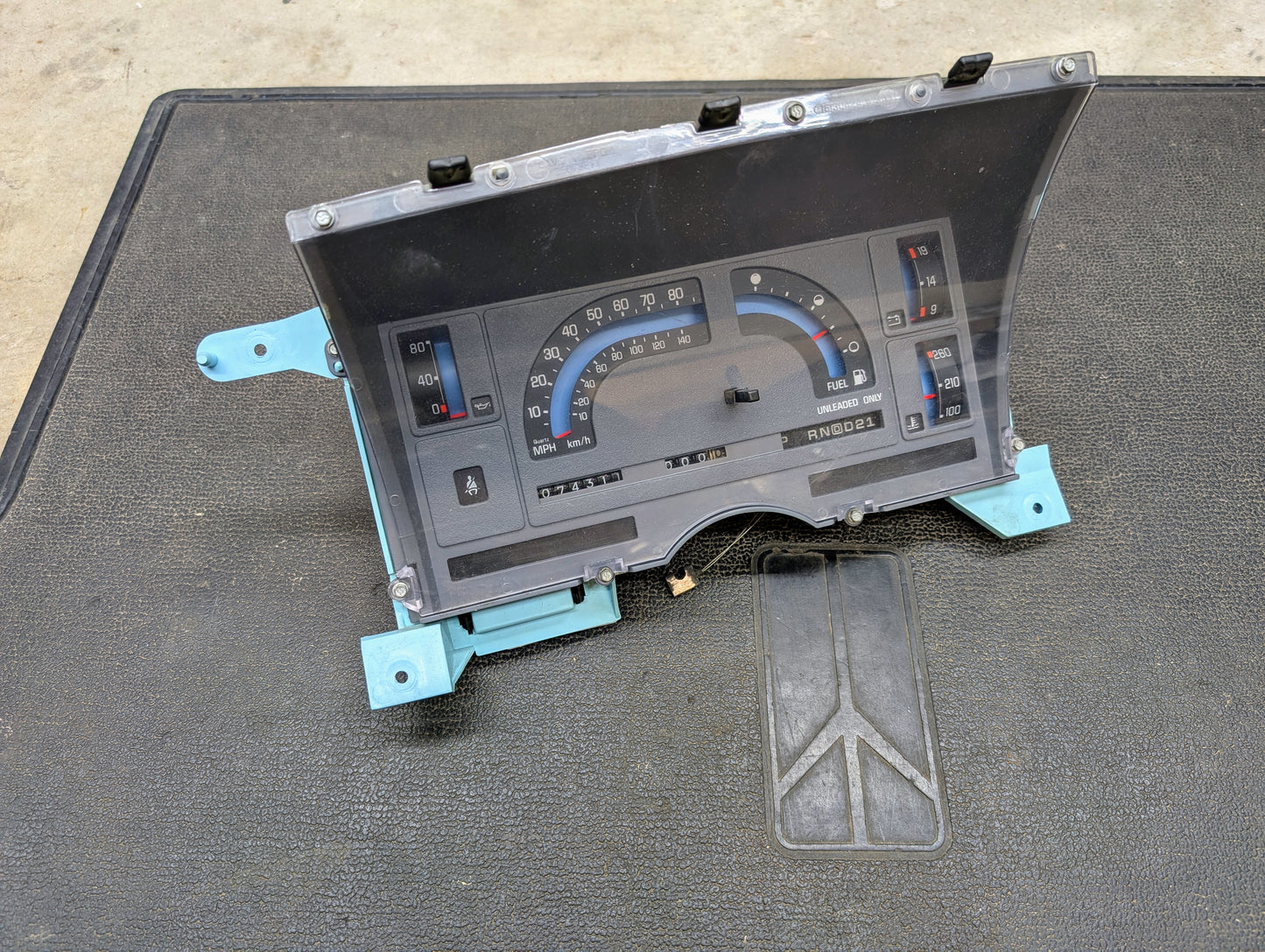 A General Motors Low Mile 74K OEM Instrument Cluster with PRNDL for 1986-1994 Chevy S10 Blazer and more is shown on a black textured surface, featuring speedometer, fuel gauge, temperature gauge, and odometer.