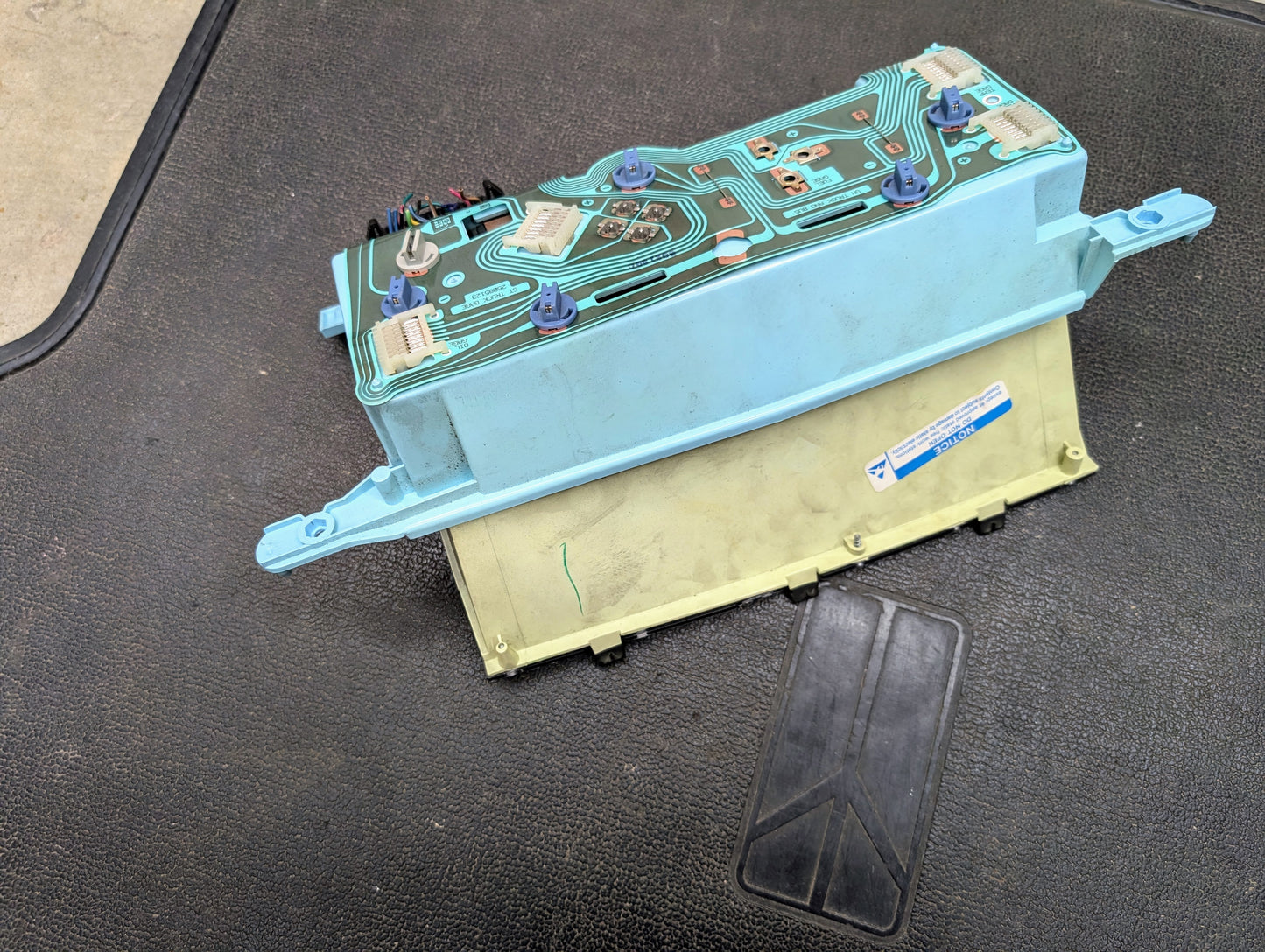A Low Mile 74K OEM Instrument Cluster with PRNDL by General Motors for 1986-1994 Chevy S10 Blazer and more is displayed on a textured black surface, revealing its blue-green printed circuit board, electronic components, and connectors.