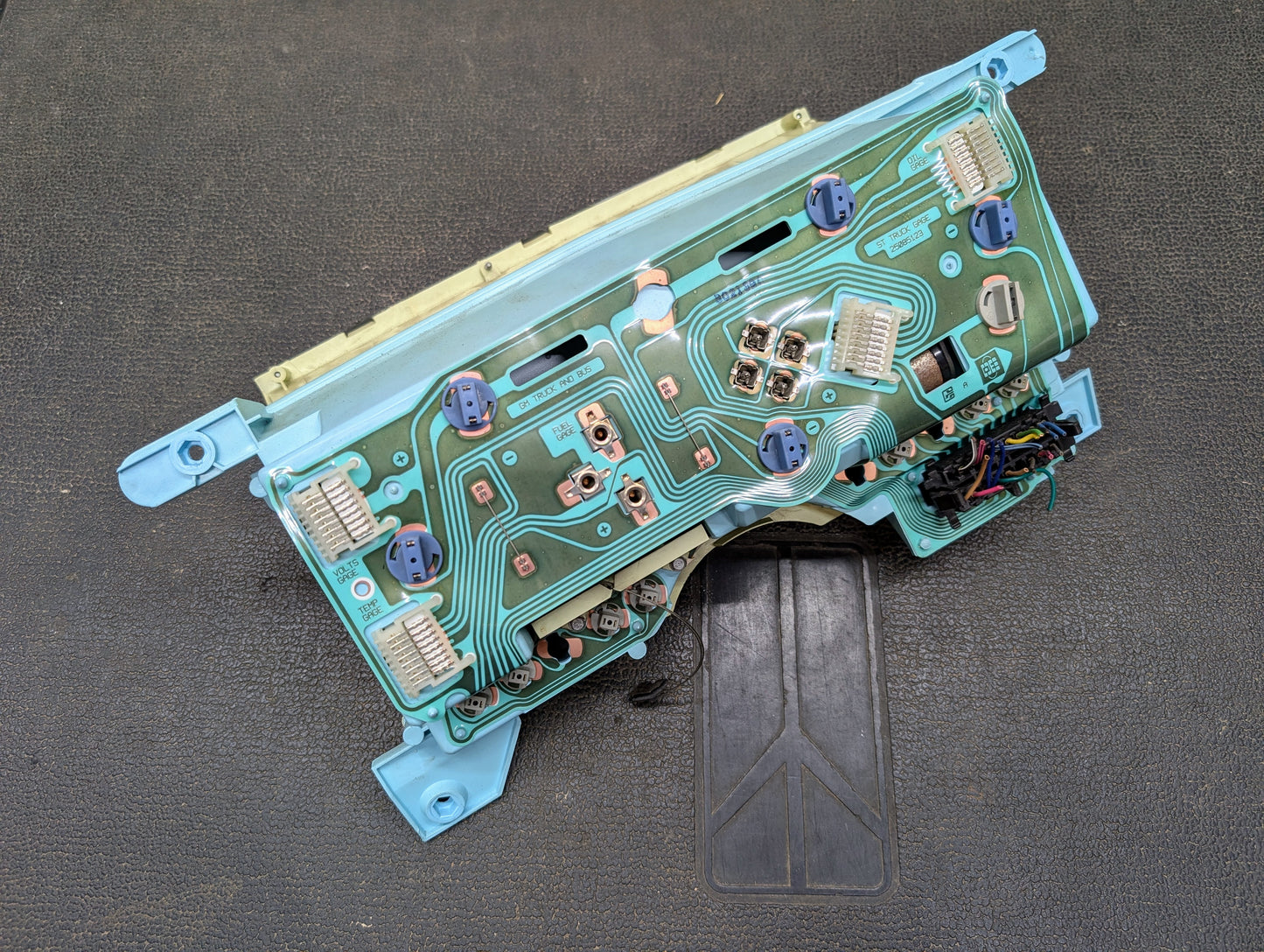 Close-up of a General Motors Low Mile 74K OEM Instrument Cluster with PRNDL for 1986-1994 Chevy S10 Blazer, featuring green wiring and connectors, displayed on a textured dark surface.