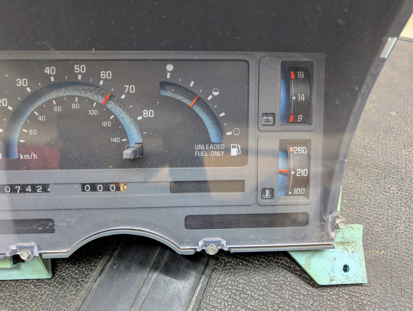 Close-up of a General Motors Low Mile 107K OEM Instrument Cluster for 1986-1994 Chevy S10 Blazer shows its analog gauges, including speedometer at zero, odometer, temperature, and UNLEADED FUEL ONLY fuel gauge reading empty.