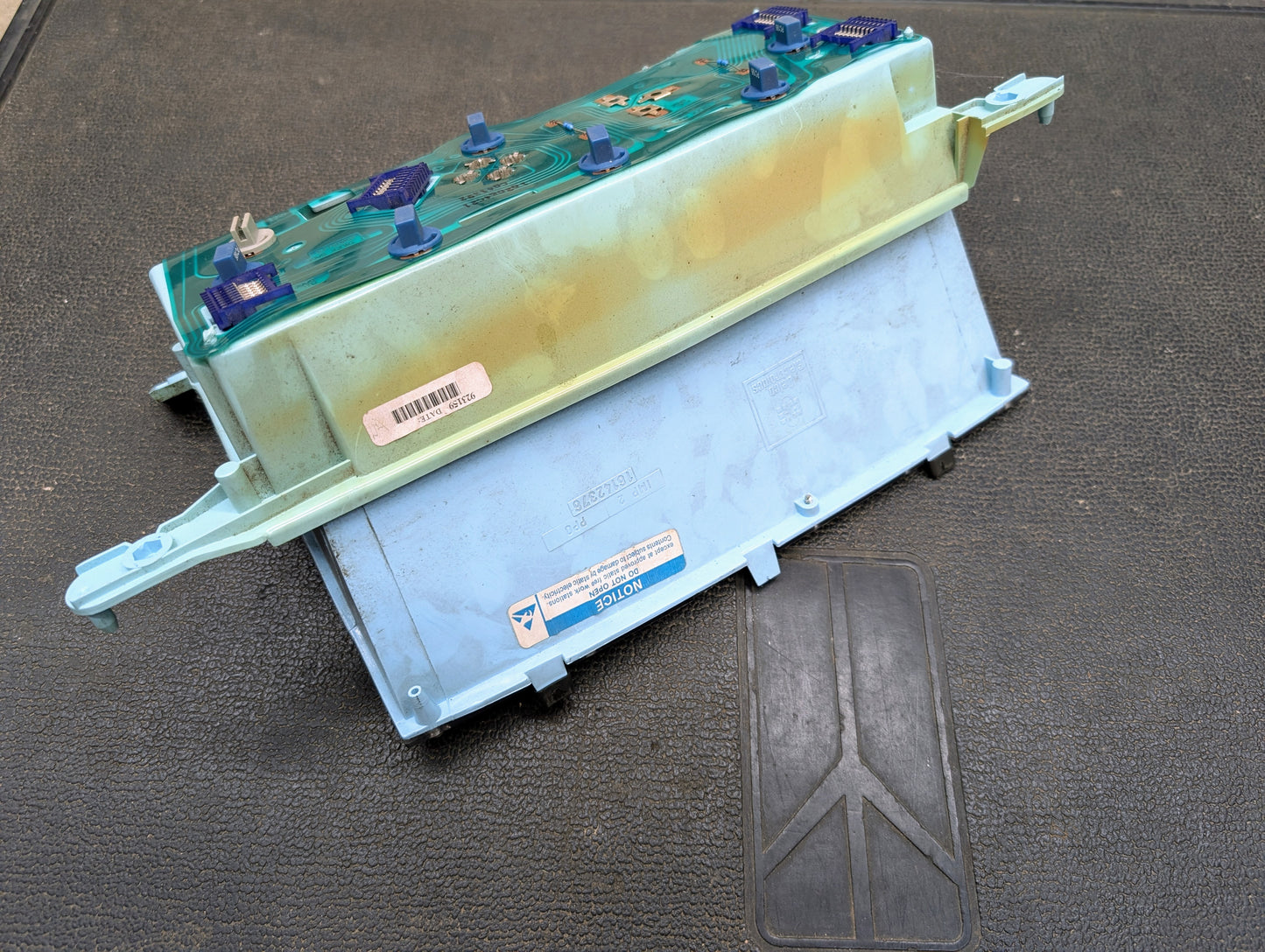 A Low Mile 107K OEM Instrument Cluster by General Motors for 1986-1994 Chevy S10 Blazer and more, with connectors, barcode label, and NOTICE sticker, part number 16142385, sits on a textured surface showing some wear.