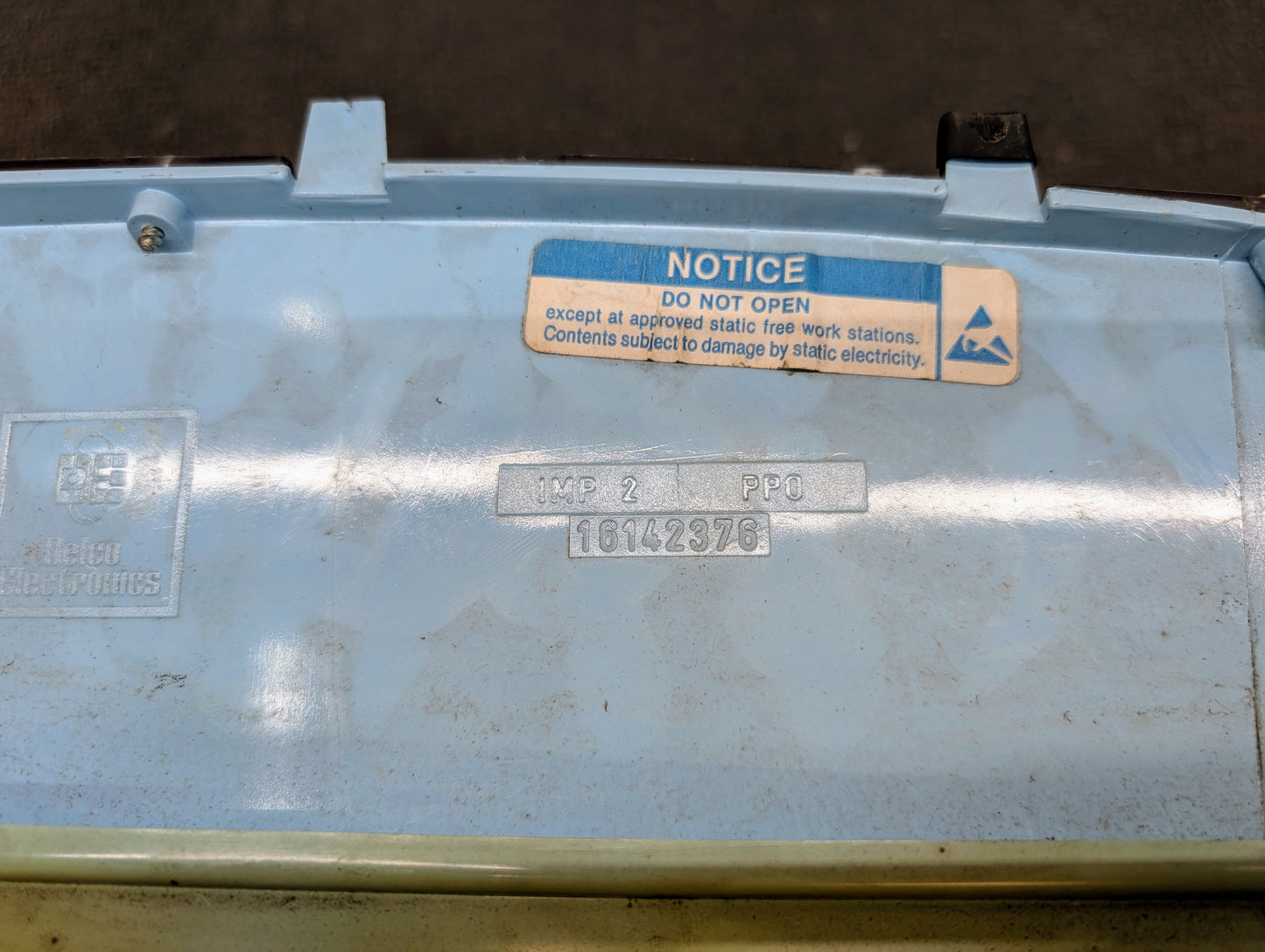 Close-up of a light blue plastic panel from a General Motors Low Mile 107K OEM Instrument Cluster for 1986-1994 Chevy S10 Blazer, featuring a white and blue NOTICE DO NOT OPEN static warning plus serial 10142976 and code 16142385.