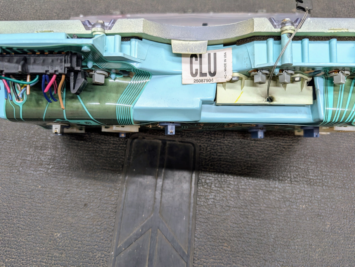 A close-up of a General Motors Low Mile 74K OEM Instrument Cluster with PRNDL for 1986-1994 Chevy S10 Blazer shows wiring, connectors, a CLU label, and a screwdriver on a screw, all against a textured black background.