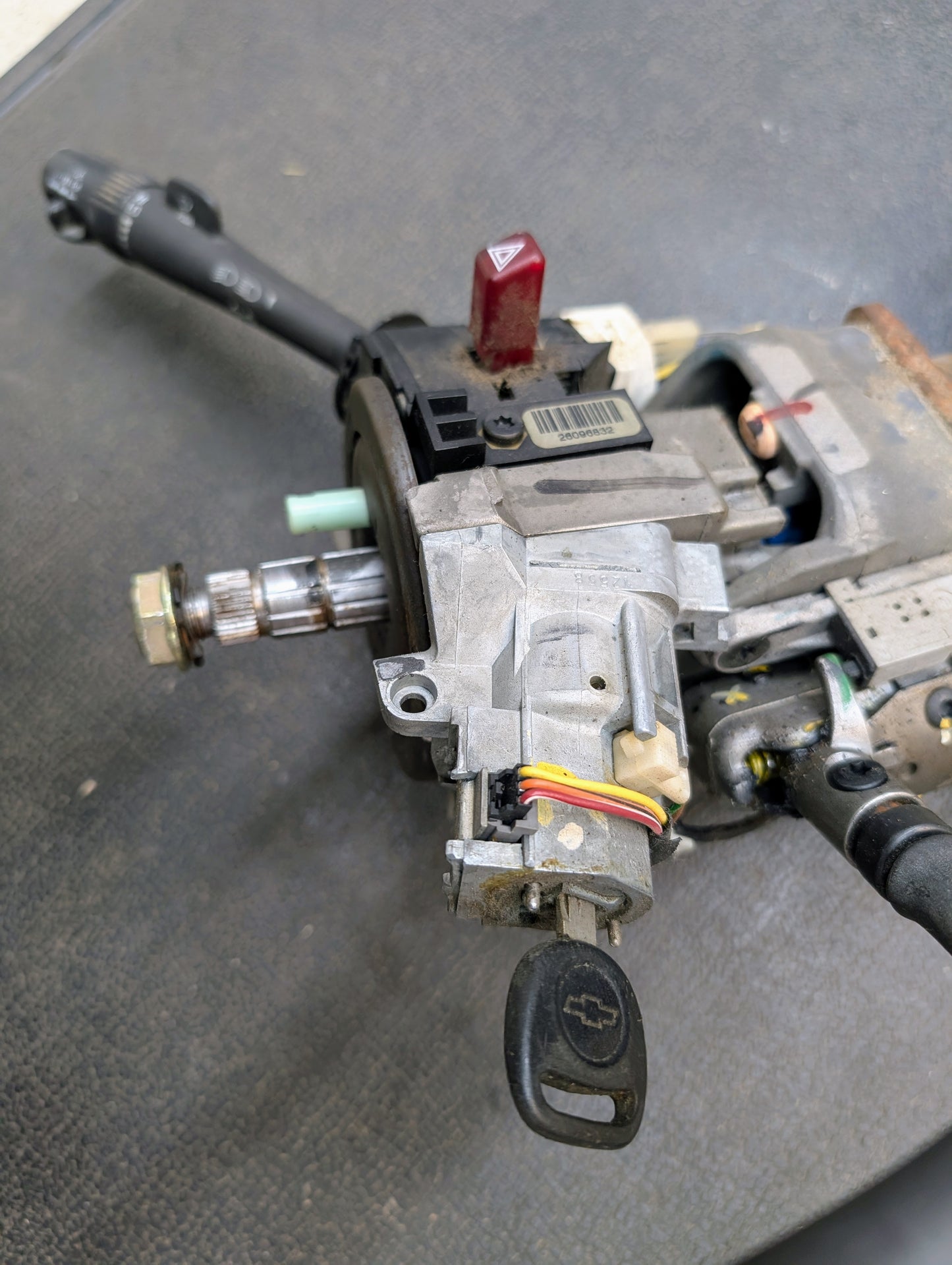 A close-up of a General Motors OEM Steering Column w/ Tilt, Cruise Control, and Column Shift for 1998-2005 Chevy S10 Blazer shows the ignition switch assembly, key inserted, colored wires, lever, and red hazard light button.
