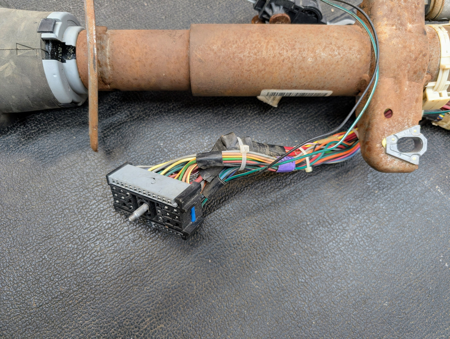 Close-up of a General Motors OEM Steering Column with Tilt, Cruise Control, and Column Shift for 1998-2005 Chevy S10/Blazer, showing exposed multicolored wiring harness and connector on a textured black surface.