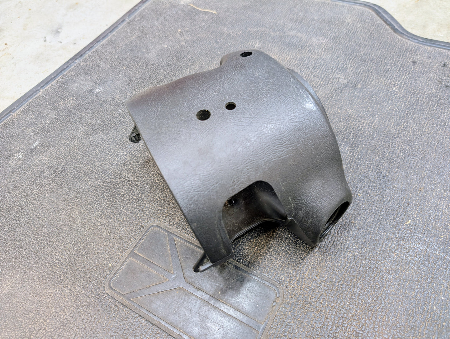 A black General Motors OEM steering column with tilt, cruise control, and column shift for 1998-2005 Chevy S10 Blazer sits on a textured rubber mat. The part appears slightly worn and is photographed at an angle from above.