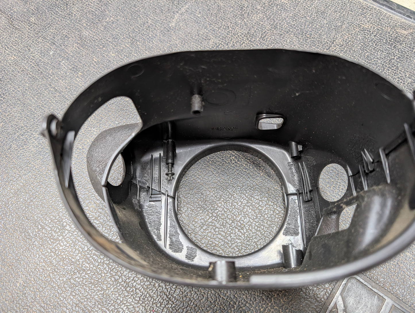 Close-up of a black General Motors OEM Steering Column w/Tilt, Cruise Control, and Column Shift for 1998-2005 Chevy S10 Blazer. The part features several openings, internal ridges, and includes a visible silver screw on a textured gray surface.