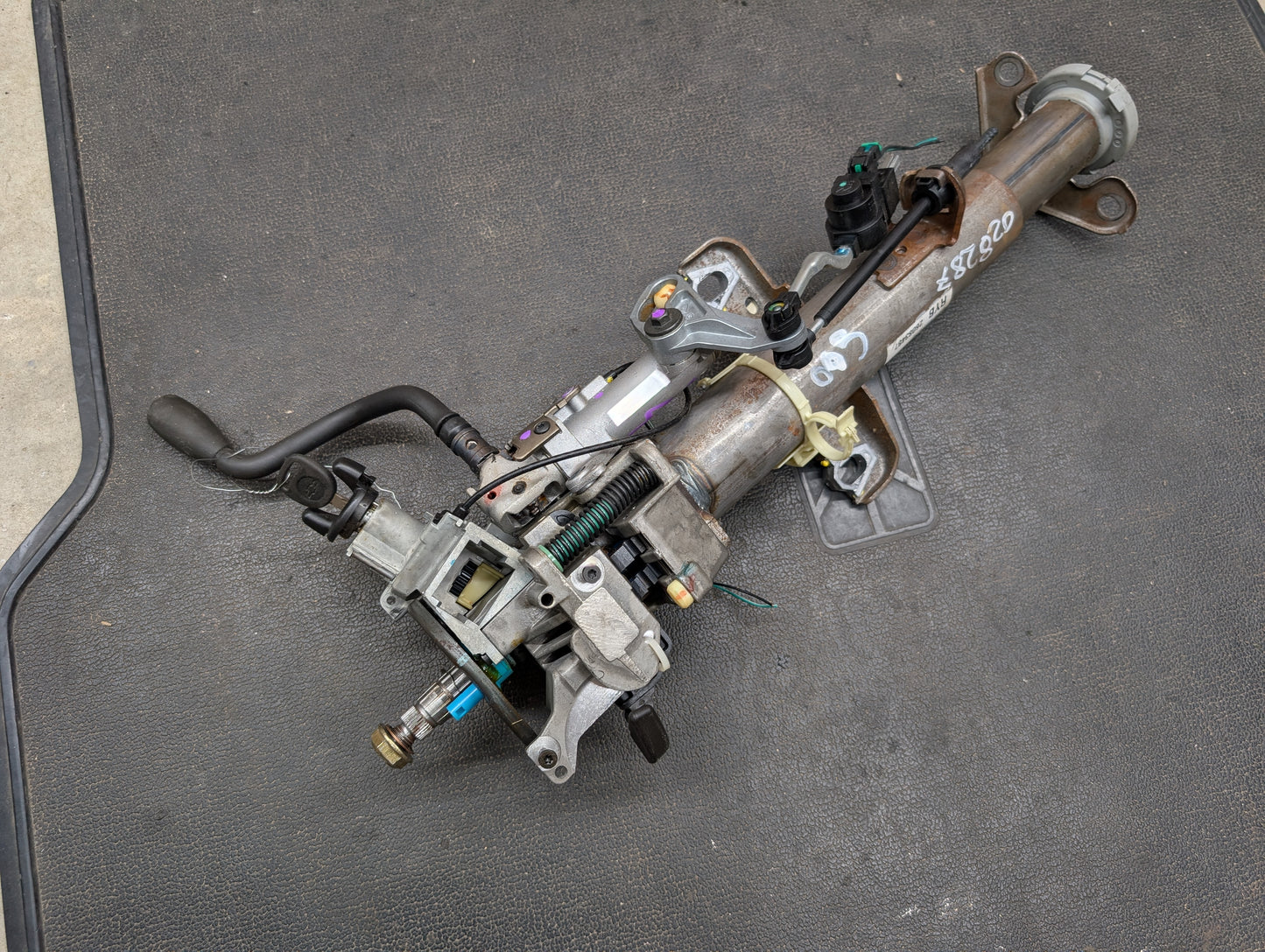 A General Motors OEM Steering Column with tilt, cruise control, and column shift for 1998-2005 Chevy S10 Blazer and more, featuring attached wiring and levers, is shown on a black mat—ideal for Blazer automatic transmissions.
