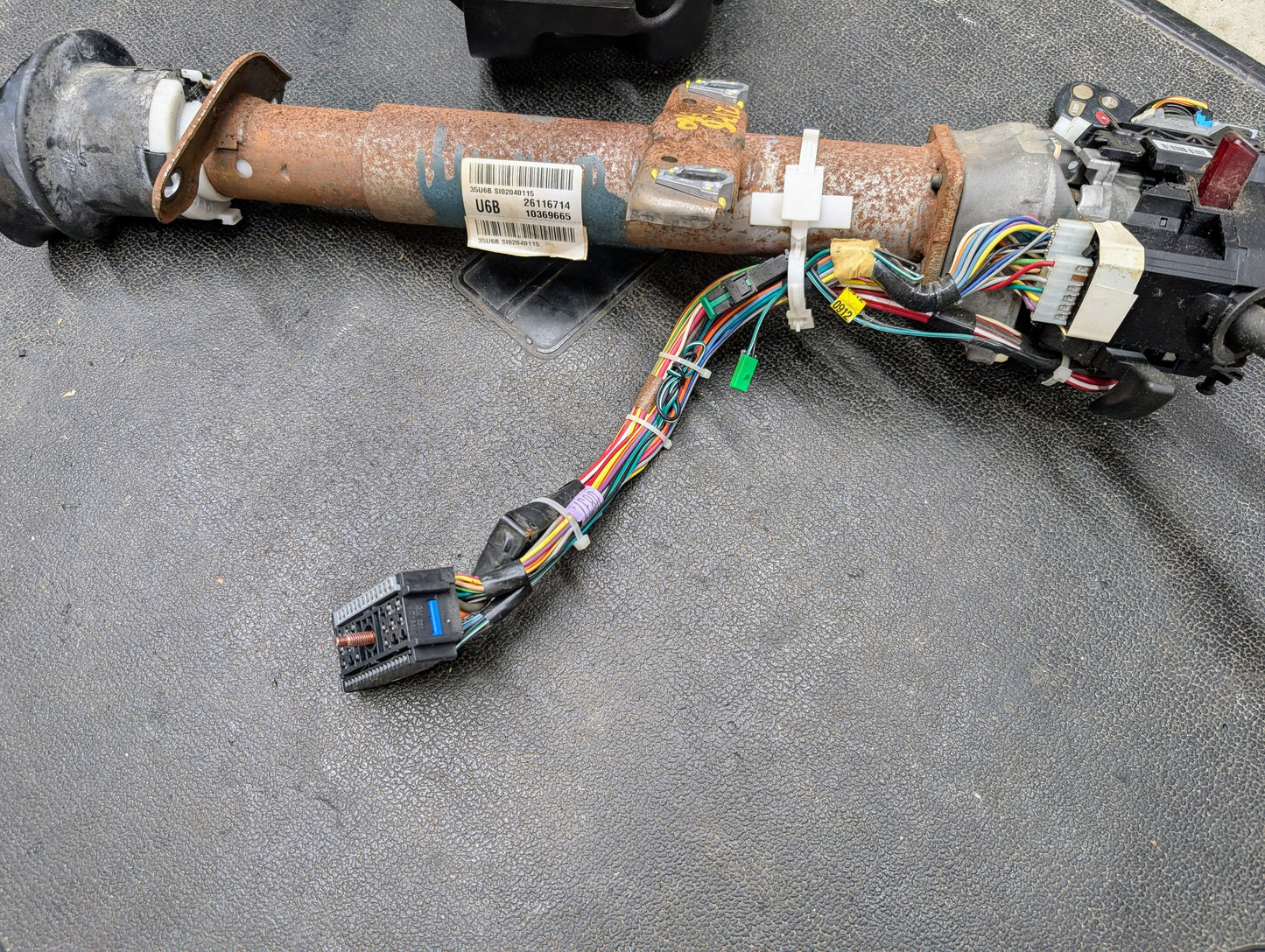 A General Motors OEM Steering Column with tilt, cruise control, and console shift for 1998-2005 Chevy S10/Blazer, including wiring harnesses, connectors, and plastic components, shown on a textured black surface.