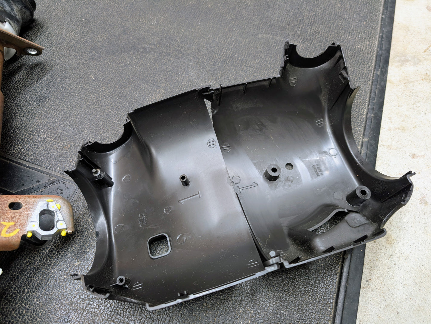 A General Motors OEM Steering Column with tilt, cruise control, and console shift for 1998-2005 Chevy S10 Blazer is shown on a textured black surface beside a partially visible tool and metal part.