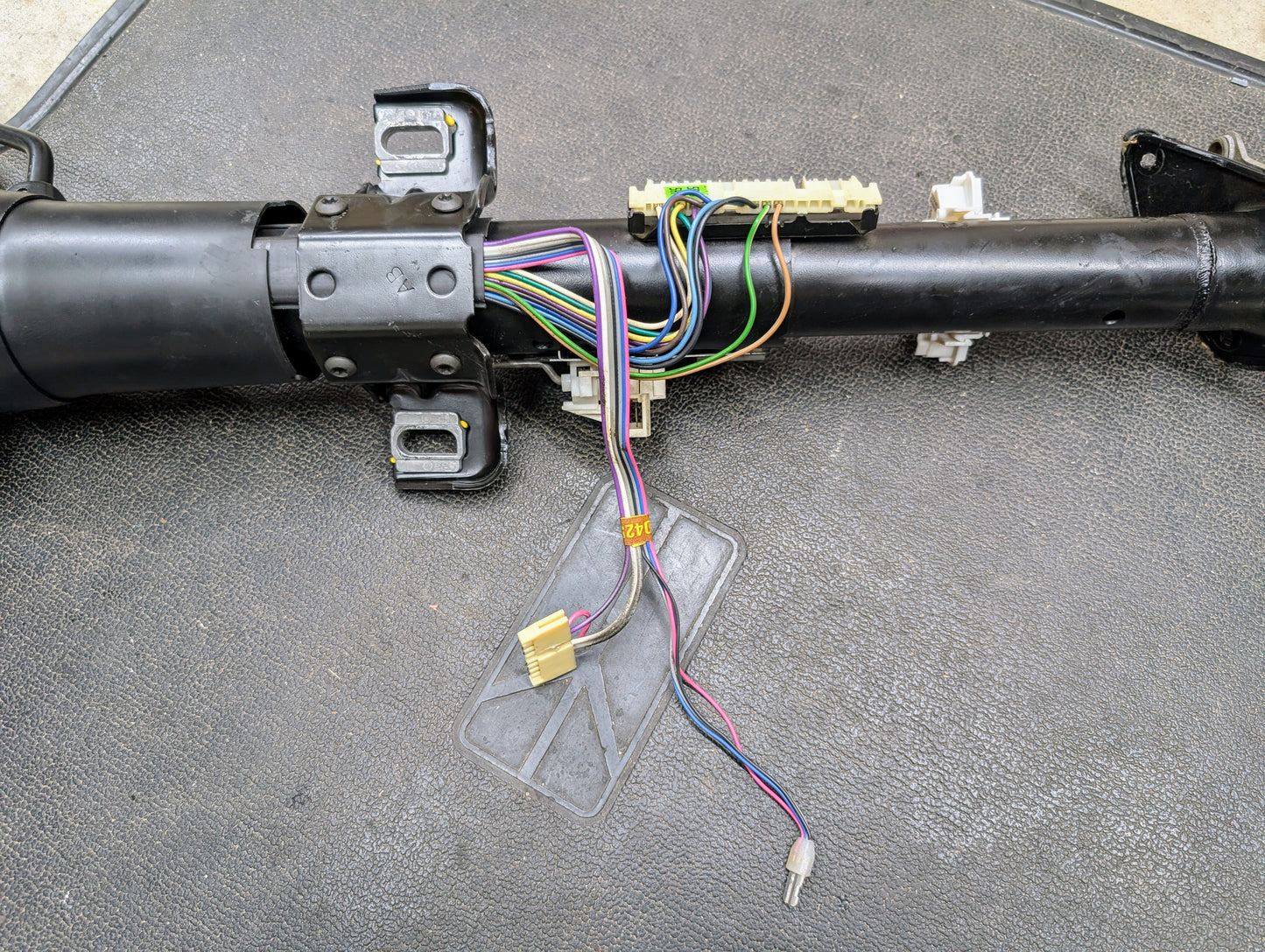 A General Motors OEM Steering Column with tilt and cruise control for 1988-1993 Chevy S10, Blazer, and more sits on a textured dark surface, showing exposed multicolored wires and connectors.