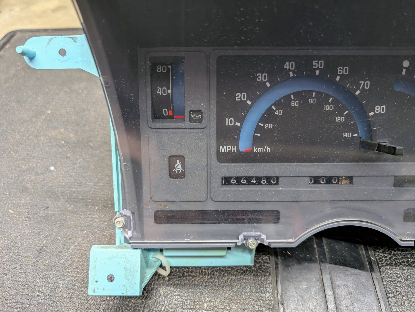 Close-up of a General Motors OEM Instrument Cluster for 1986-1994 Chevy S10 Blazer, featuring the speedometer in MPH/km/h, odometer at 166480, and oil/seatbelt warning lights behind a clear plastic cover.