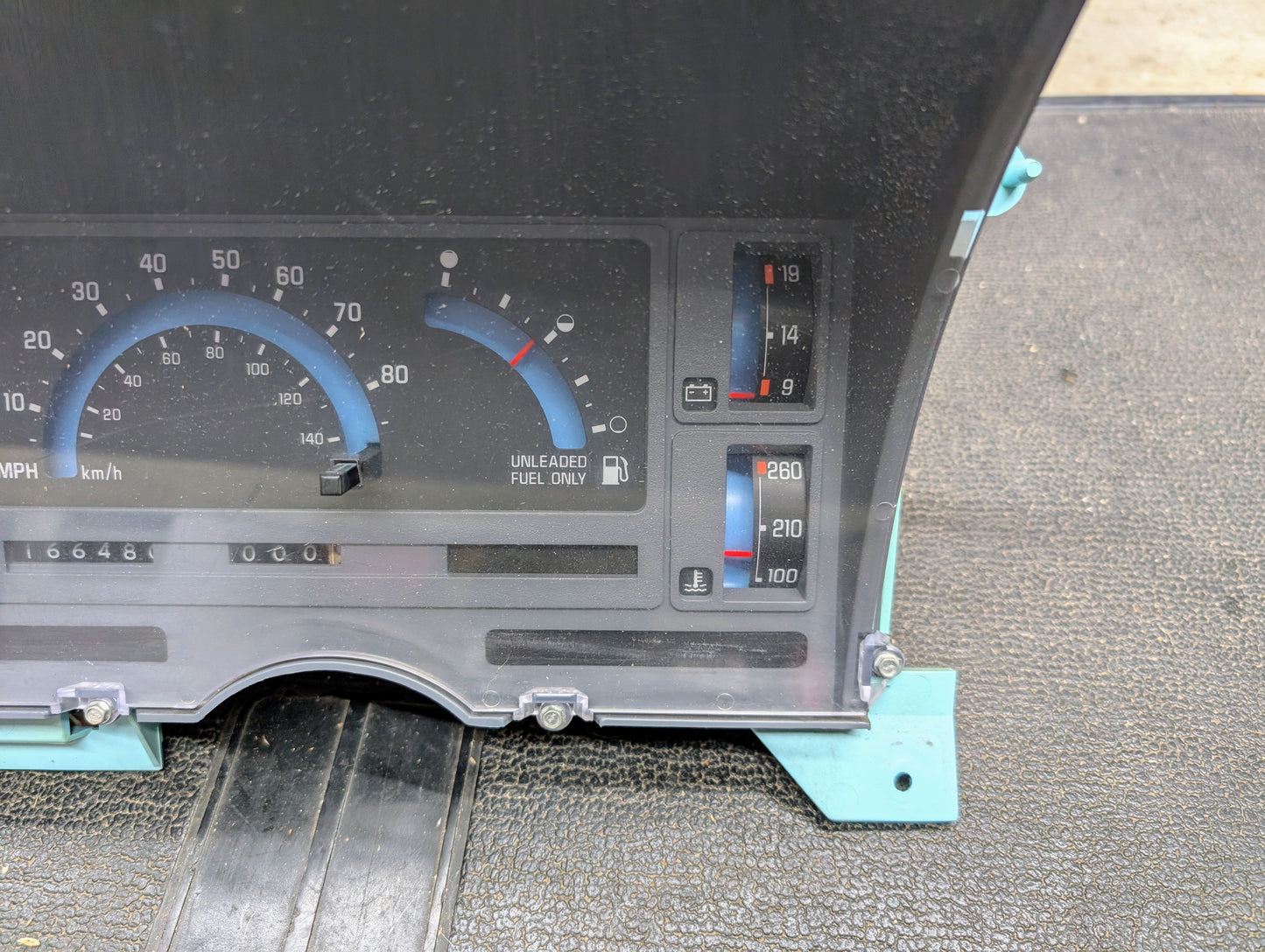 A close-up of a General Motors OEM Instrument Cluster for 1986-1994 Chevy S10 Blazer, featuring analog speedometer, fuel, and temperature gauges removed and placed on a textured surface.