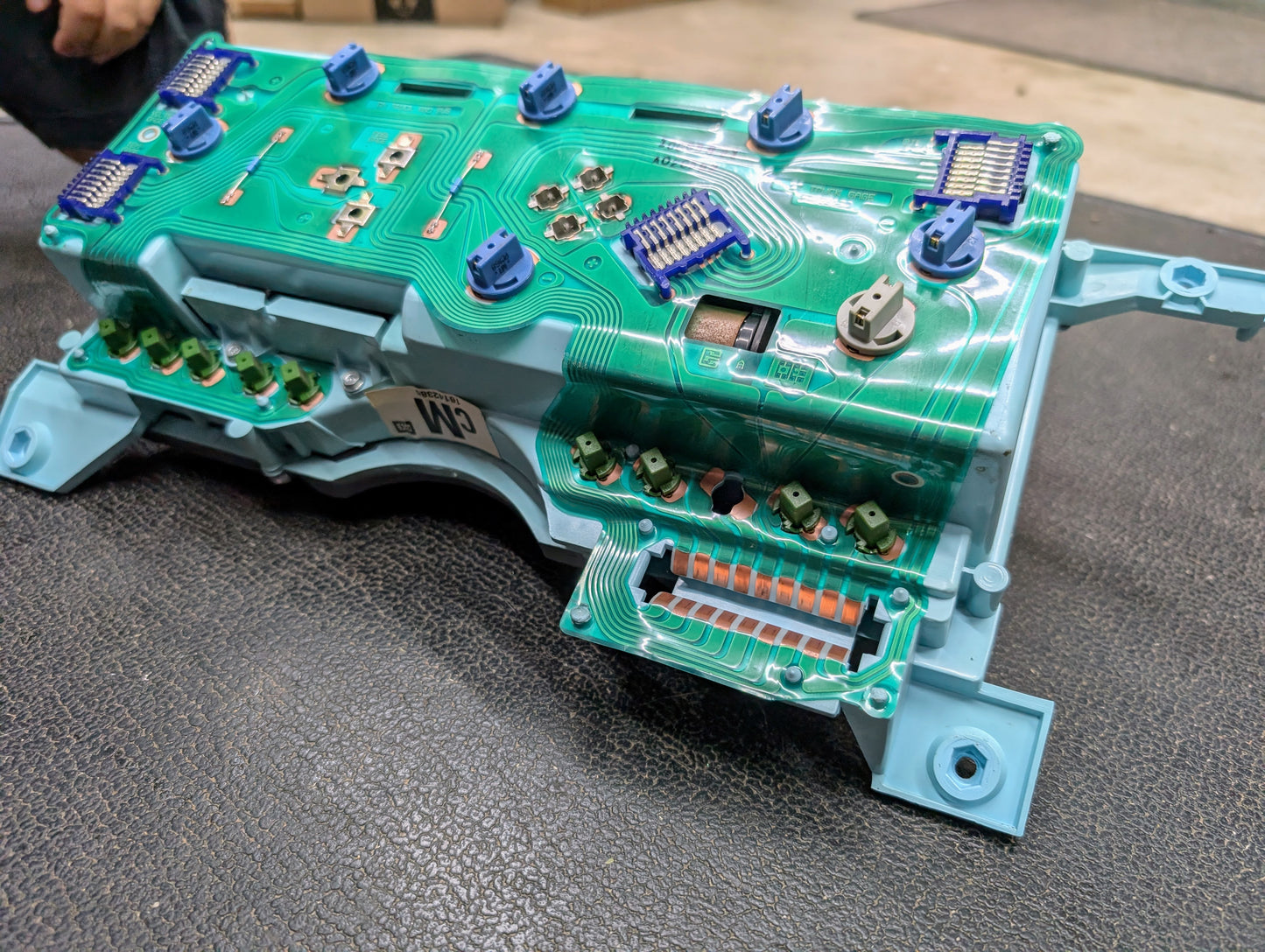 A close-up of a General Motors OEM Instrument Cluster for 1986-1994 Chevy S10 Blazer and more, featuring green wiring, blue and white connectors, and electronic components on a textured black surface.