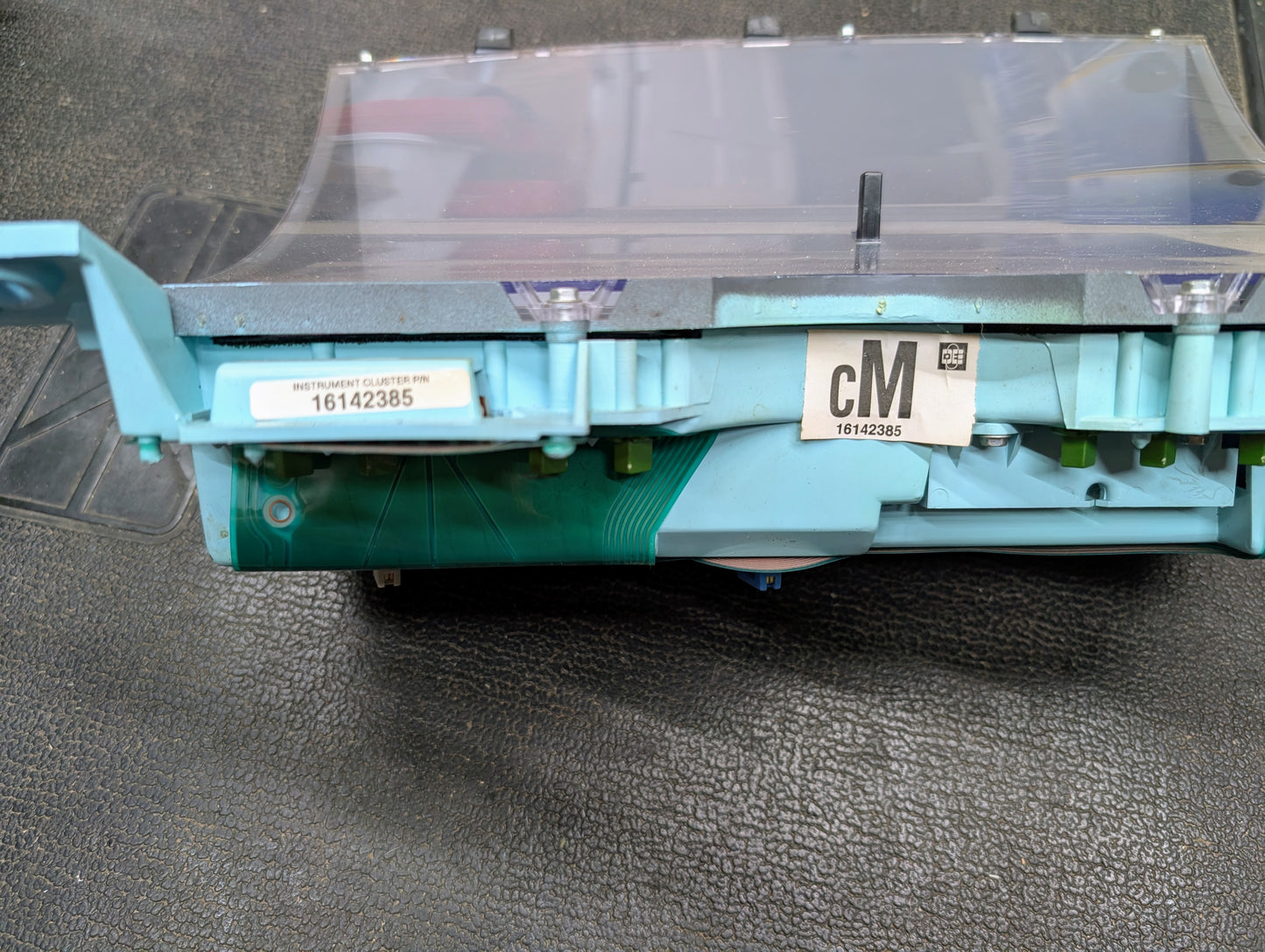 A close-up of a General Motors OEM Instrument Cluster for 1986-1994 Chevy S10 Blazer shows labels “INSTRUMENT CLUSTER P/N 16142385” and “cM 16142385,” with the analog circuit board and plastic parts visible on a textured black surface.