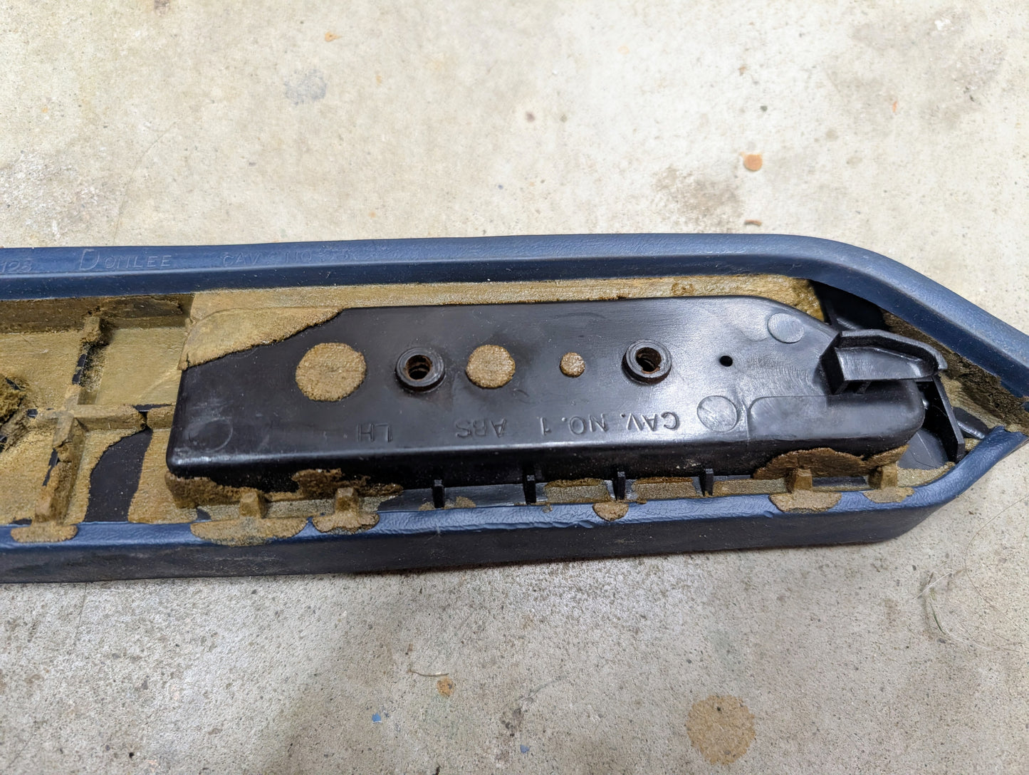 A close-up of a blue OEM driver door panel armrest handle by General Motors for 1986-1993 Chevy S10 and Blazer, resting on a rough beige surface.