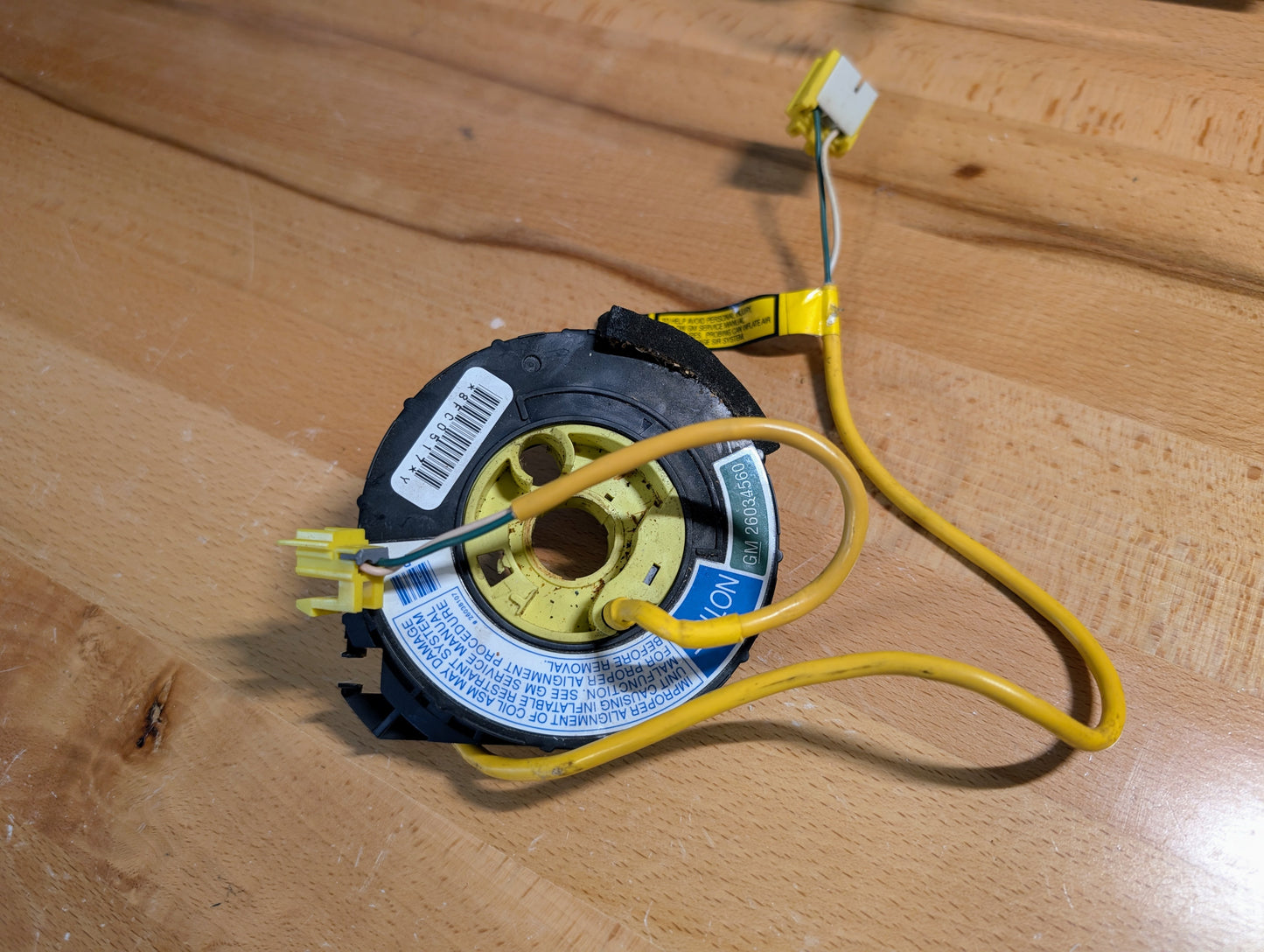 A General Motors OEM TESTED Steering Wheel SRS Air Bag Clock Spring for 1995-1998 Chevy S10 and C/K Truck features yellow wires, connectors, warning labels, and barcodes resting on a wooden surface.