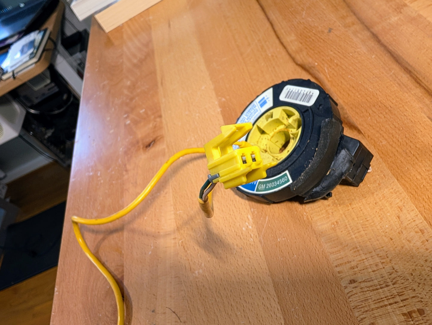 A General Motors TESTED Steering Wheel SRS Air Bag Clock Spring OEM for 1995-1998 Chevy S10 and C/K Truck is placed on a wooden workbench in a workshop.