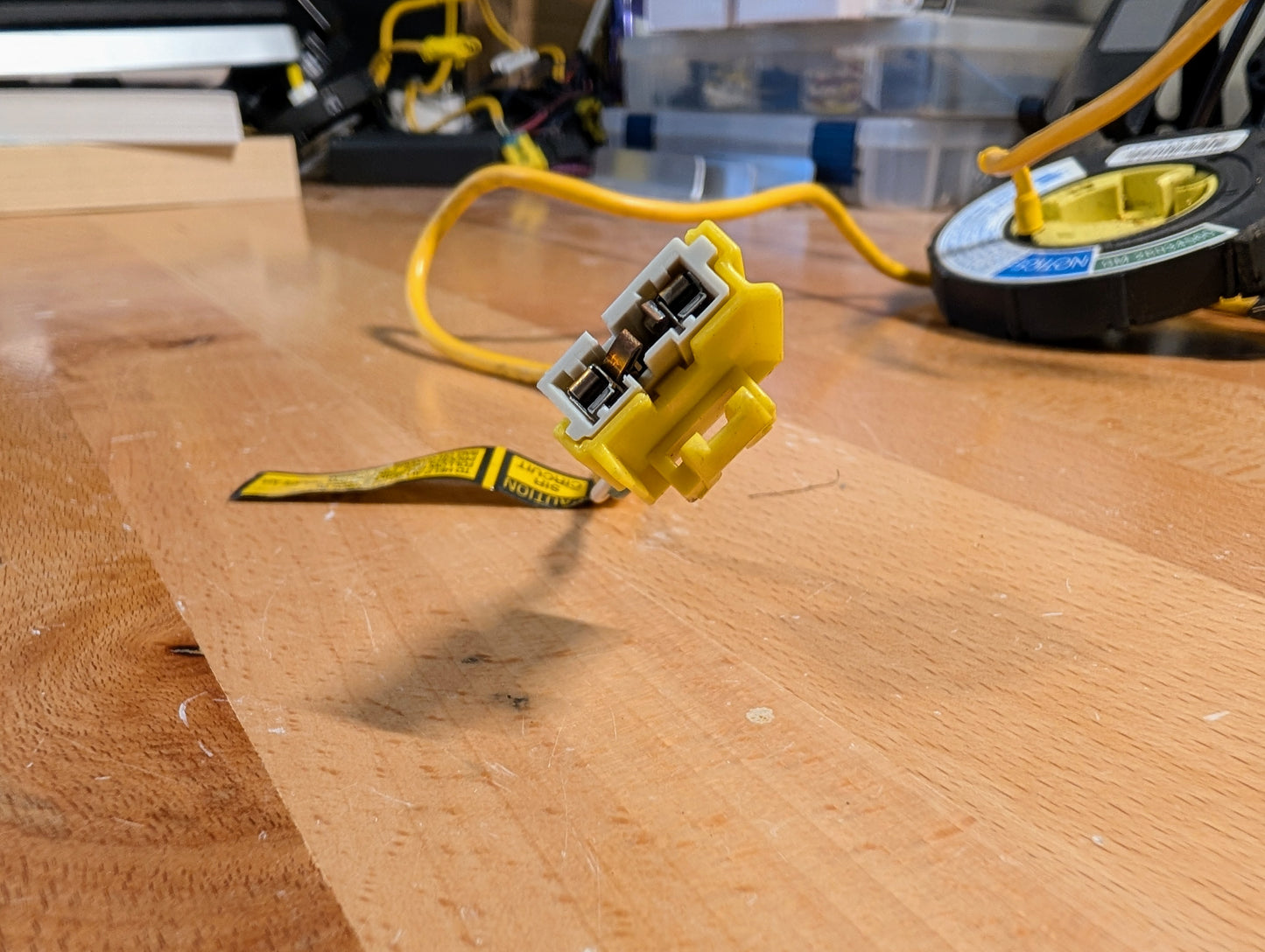 A close-up of a General Motors OEM SRS Air Bag Clock Spring for 1995-1998 Chevy S10/C/K trucks, with warning label, on a wooden workbench—yellow cable and tools in the background—ideal for GM repairs.