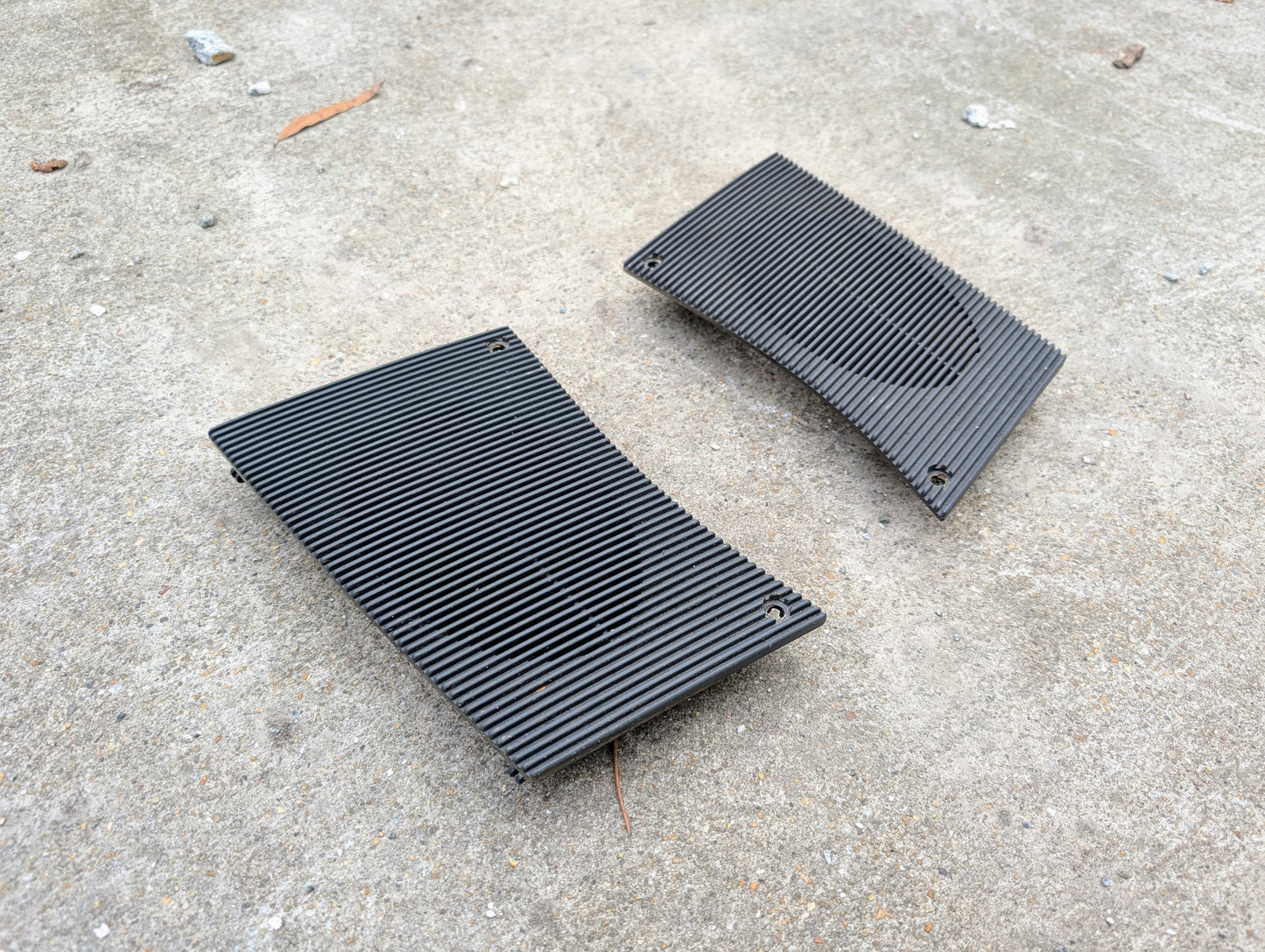Two black speaker grilles on a concrete surface