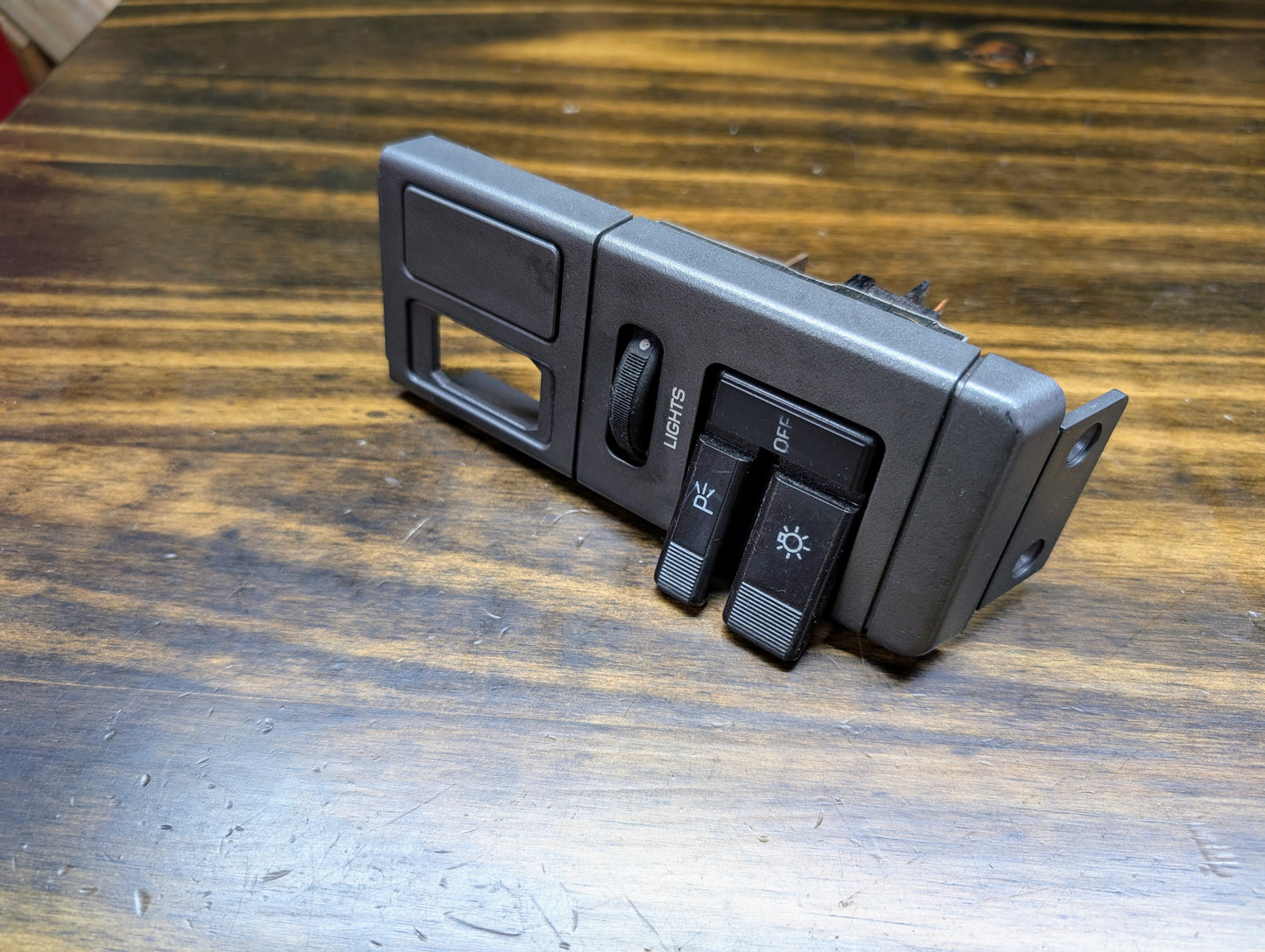 A black General Motors OEM Headlight Switch for 1986–1994 Chevy S10, Blazer, GMC S15, Jimmy with levers labeled P and Lights, is shown on a wooden surface.