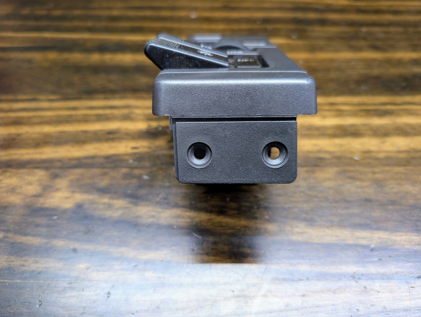 Close-up of a General Motors OEM Headlight Headlamp Switch for 1986-1994 Chevy S10, Blazer, GMC S15, and Jimmy—features two round holes on its side and rests on a wooden surface; perfect as a replacement part.