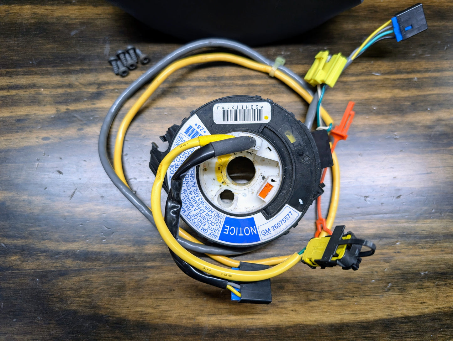 A General Motors KIT Steering Wheel Radio Controls & Clock Spring for 1999 Chevy S10, Blazer, and more rests on wood with colored wires, connectors, four screws, a barcode label, and a blue notice sticker.