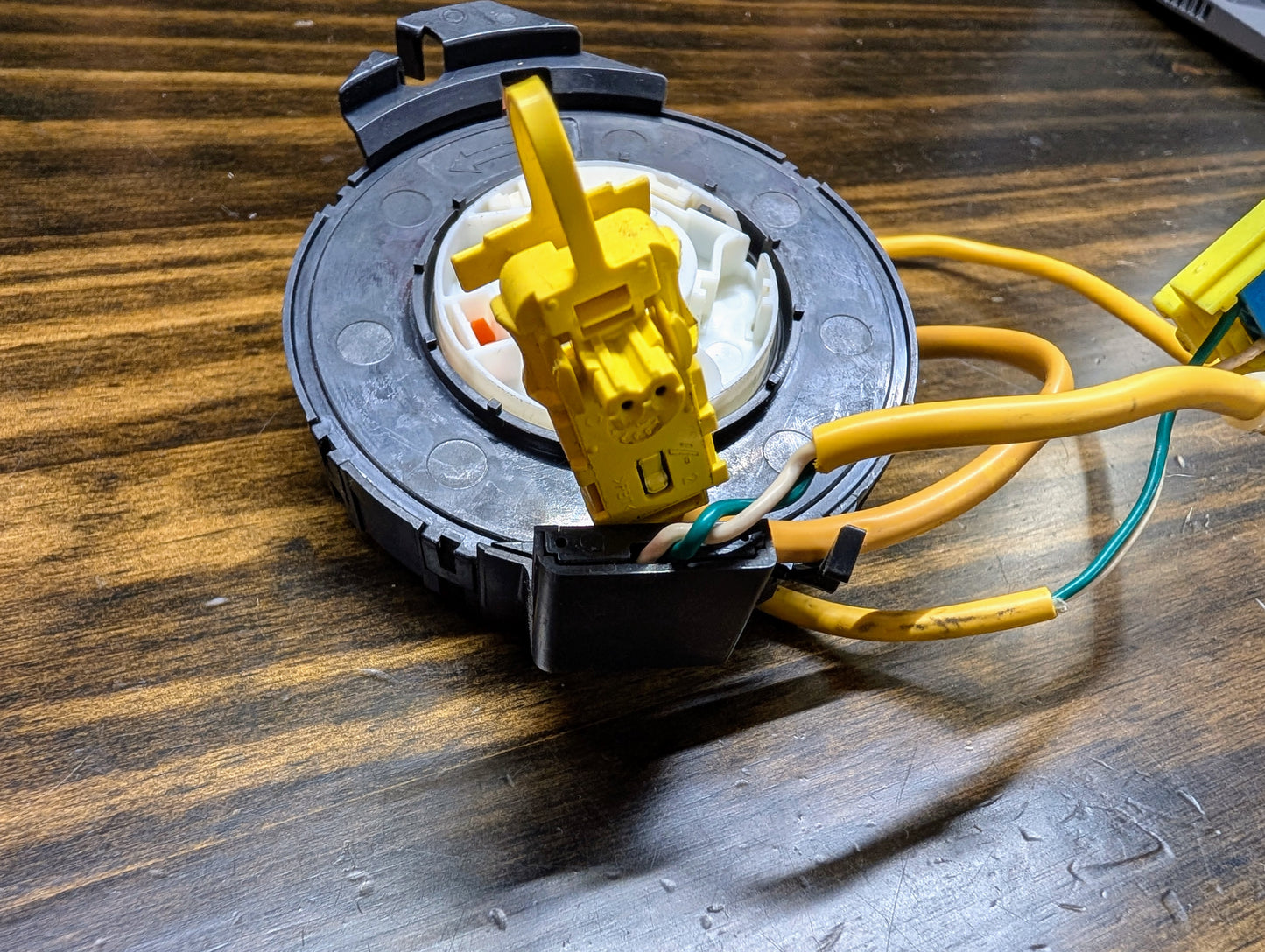 A close-up of a General Motors TESTED Steering Wheel Air Bag SRS Clock Spring OEM for 2000-2003 Chevy S10 Blazer, showing yellow and green wires with connectors and part numbers 26088306, 26087310, 26083473 on a wooden surface.