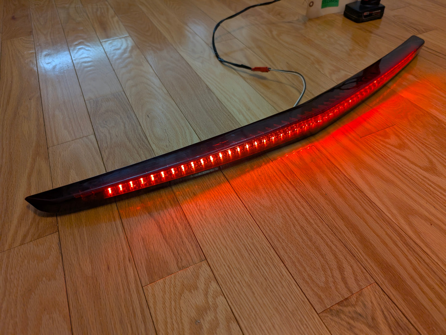 An illuminated OEM 2008-2013 Cadillac CTS Rear Stop Third Brake Light by General Motors lies on a wooden floor with visible wires, highlighting this tested CHMSL trunk lamp as a crucial exterior part for your CTS.
