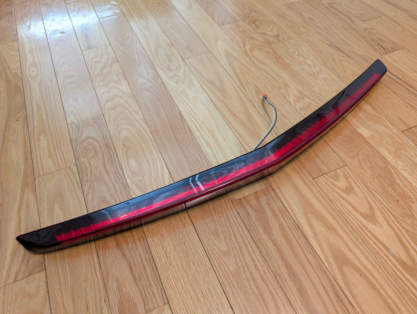 A General Motors OEM 2008-2013 Cadillac CTS Rear Stop Third Brake Light (CHMSL) is shown on a light wood floor—an essential, tested trunk lamp for Cadillac CTS sedan exterior and rear lighting.