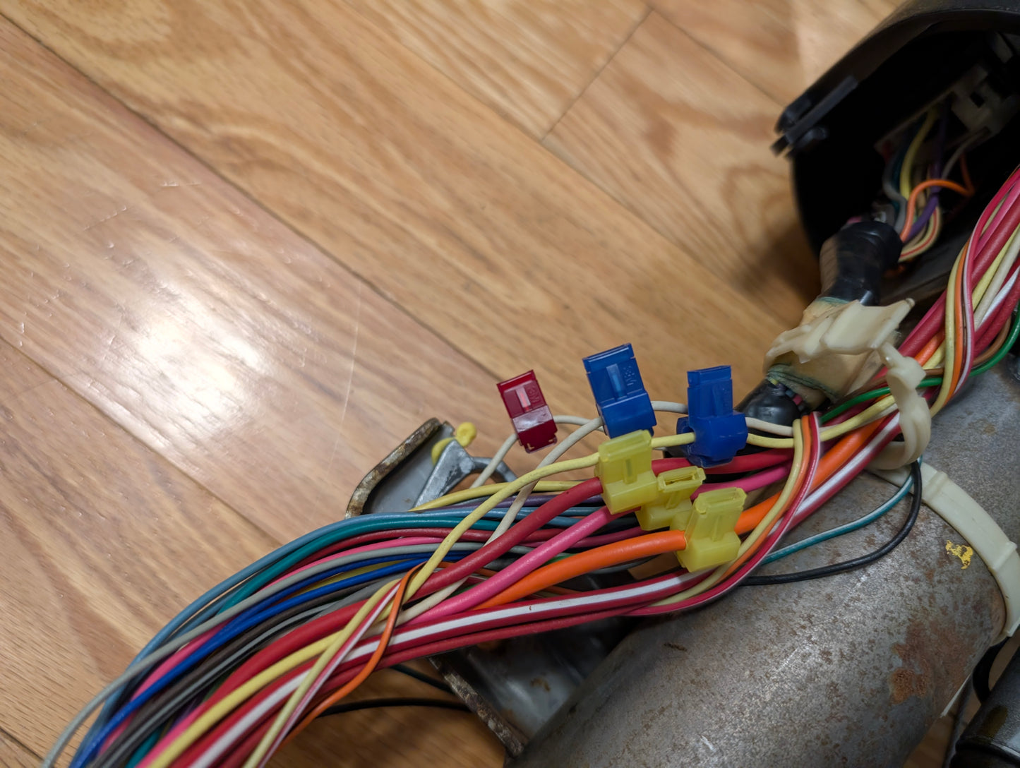 A bundle of colorful electrical wires with blue and yellow connectors and a red fuse on a wooden floor, attached to the General Motors OEM Steering Column w/Tilt, Cruise Control, and Column Shift for 1998-2005 Chevy S10 Blazer.
