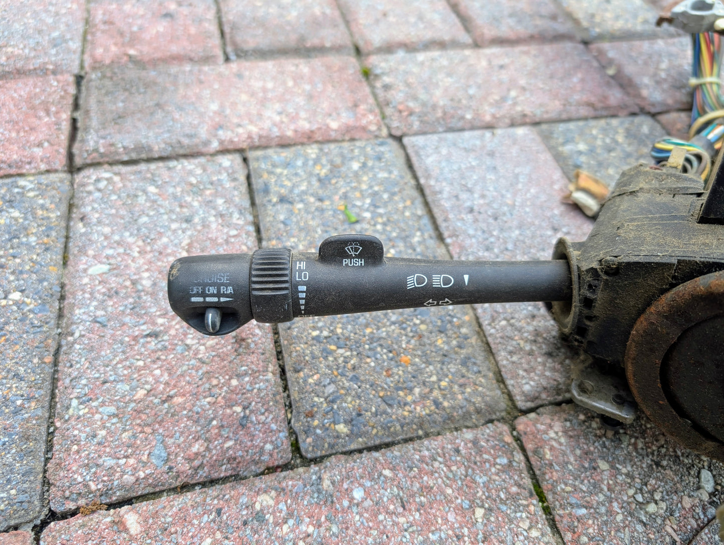 A close-up of a General Motors OEM Steering Column with tilt, cruise control, and column shift for 1998–2005 Chevy S10 Blazer shows lever assembly with symbols for lights, wipers, washer, and visible wires on the right side.