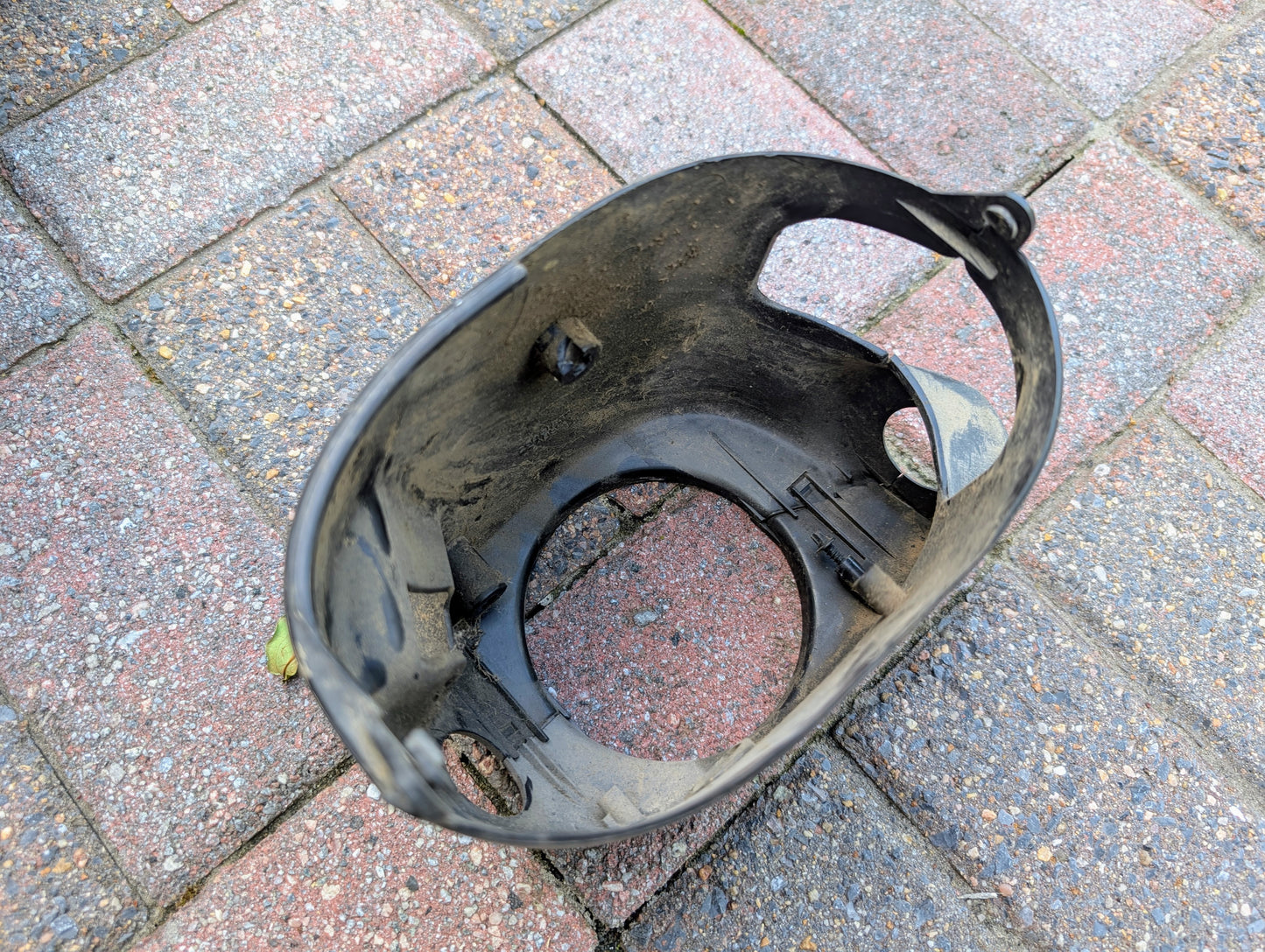 A dirty, black OEM General Motors steering column with tilt, cruise control, and column shift for 1998-2005 Chevy S10 Blazer lies on multicolored brick pavement.