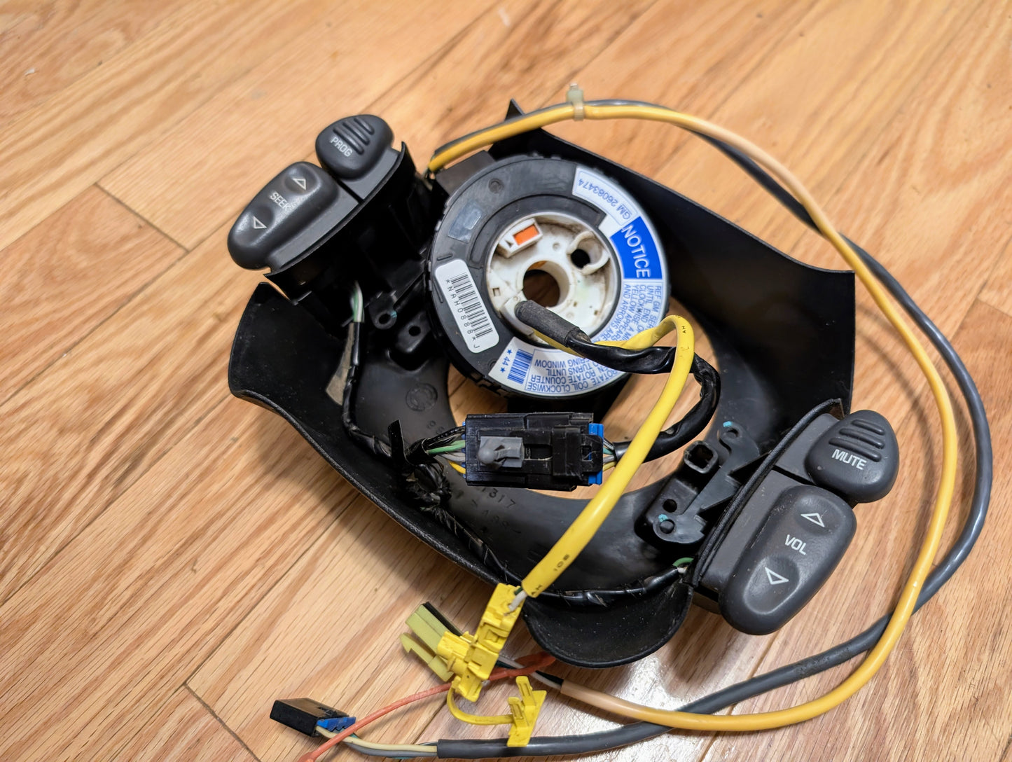 A disassembled General Motors KIT Steering Wheel Radio Controls & Clock Spring for 2000-2003 Chevy S10, Blazer, and more shows exposed volume, mute, and phone wiring and buttons on a wooden floor.