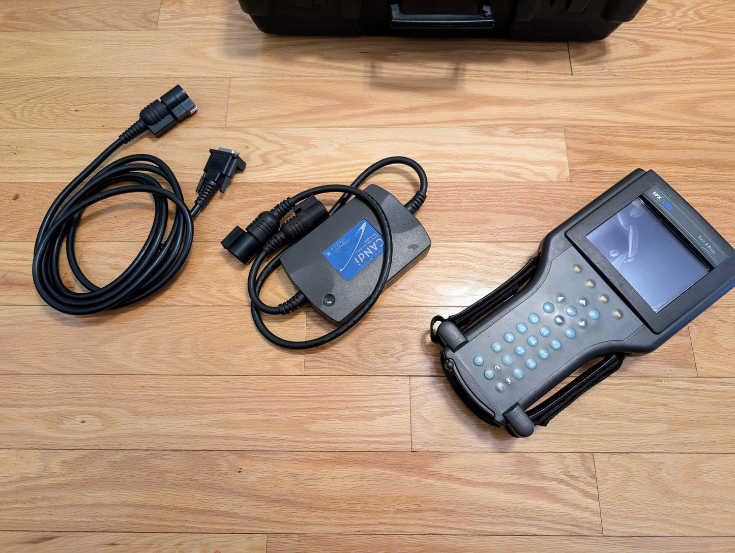 The Vetronix TESTED Tech 2 Automotive Diagnostic Tool & Accessories for 1991-2013 GM vehicles, featuring a screen, keypad, IPAW adapter, and cables, are displayed on a wooden floor—perfect for GM diagnostics and OBD2 scanning.